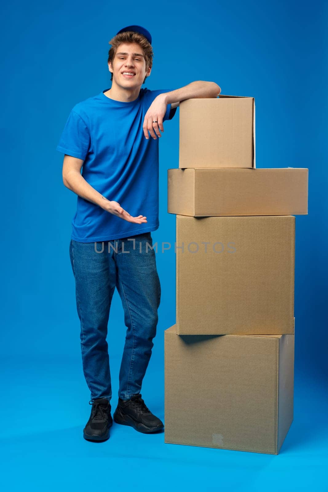 Young male courier in a blue uniform holds parcel in his hands in studio
