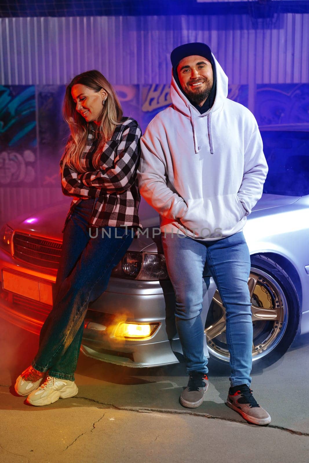 Smiling couple standing near sport car over night city background by Fabrikasimf