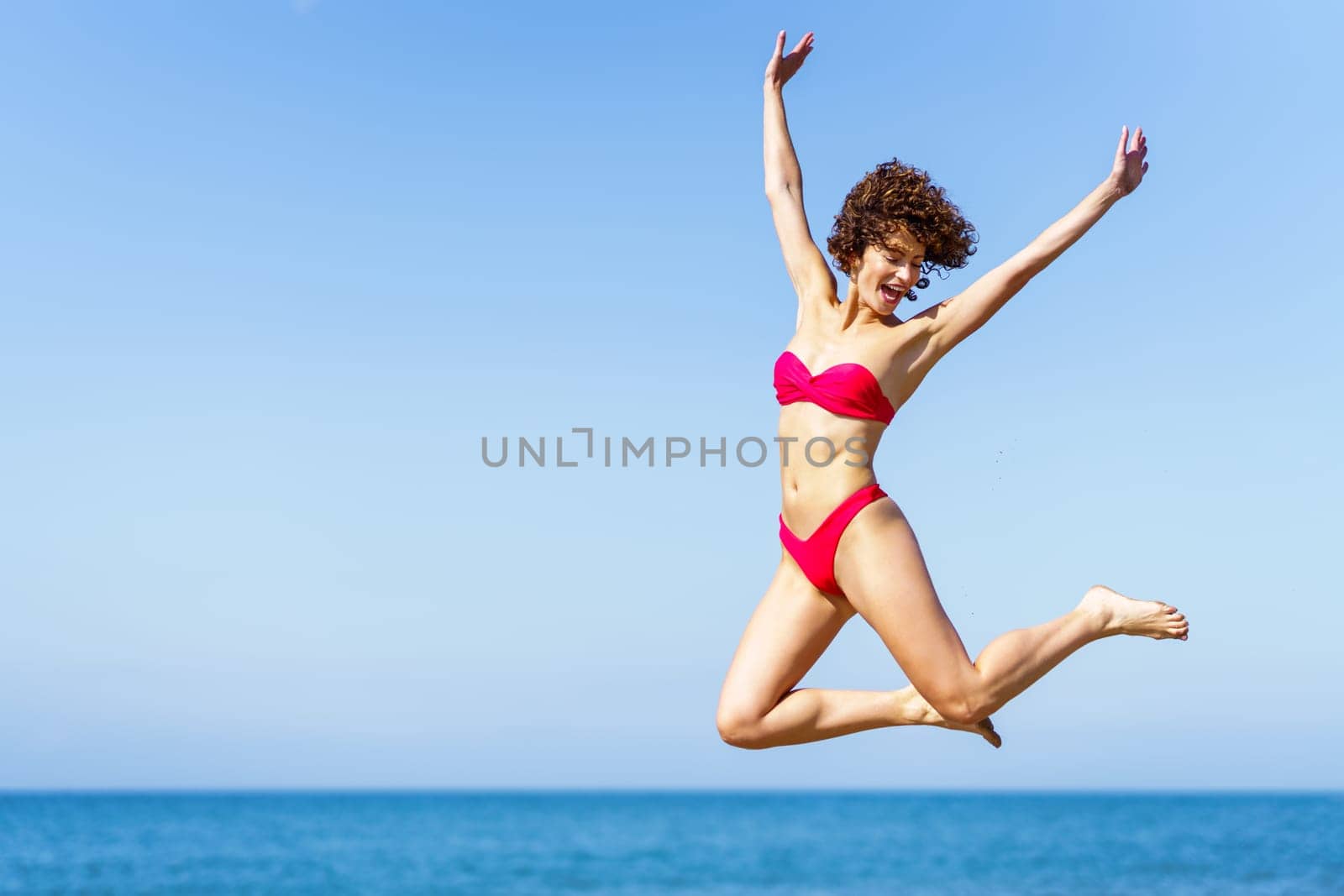 Happy woman in bikini jumping with raised arms by javiindy