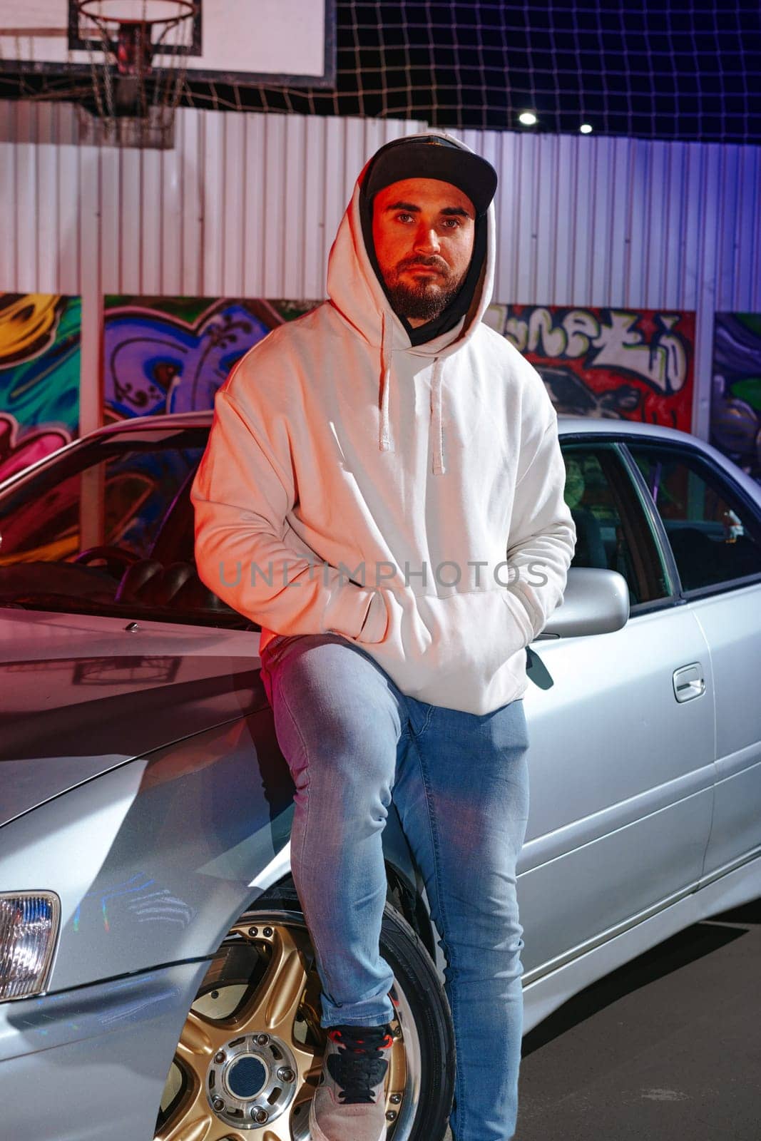 A young man standing next to his sport car at night parking in neon light