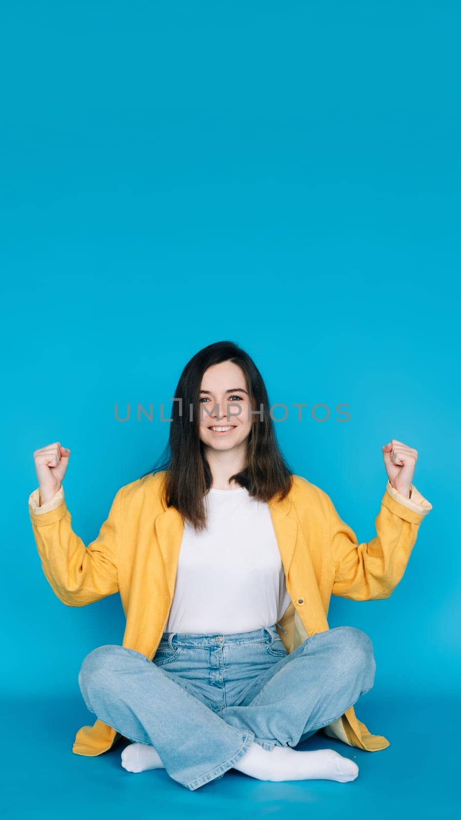 Energetic Young Woman Celebrating Success with Raised Fists, Exclaiming 'Yes ' - Vibrant Blue Background - Positive, Optimistic Concept.