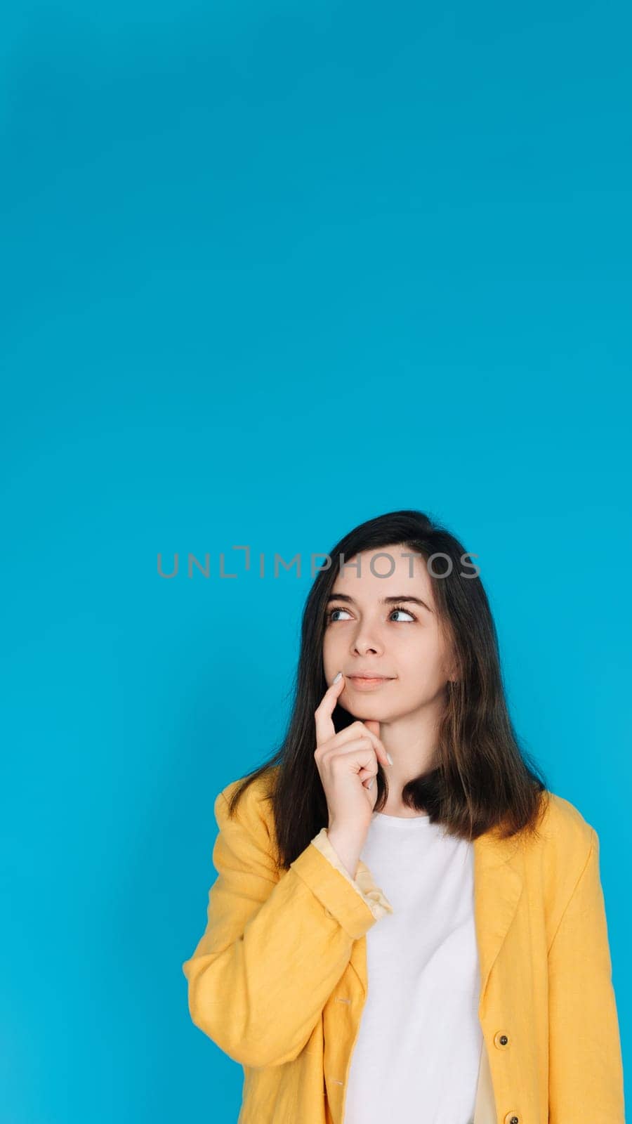 Thoughtful and Stylish Woman in Trendy Clothing - Portrait of an Attractive Young Lady with a Skeptical Gaze, Isolated on Blue Background - Copy Space Available.