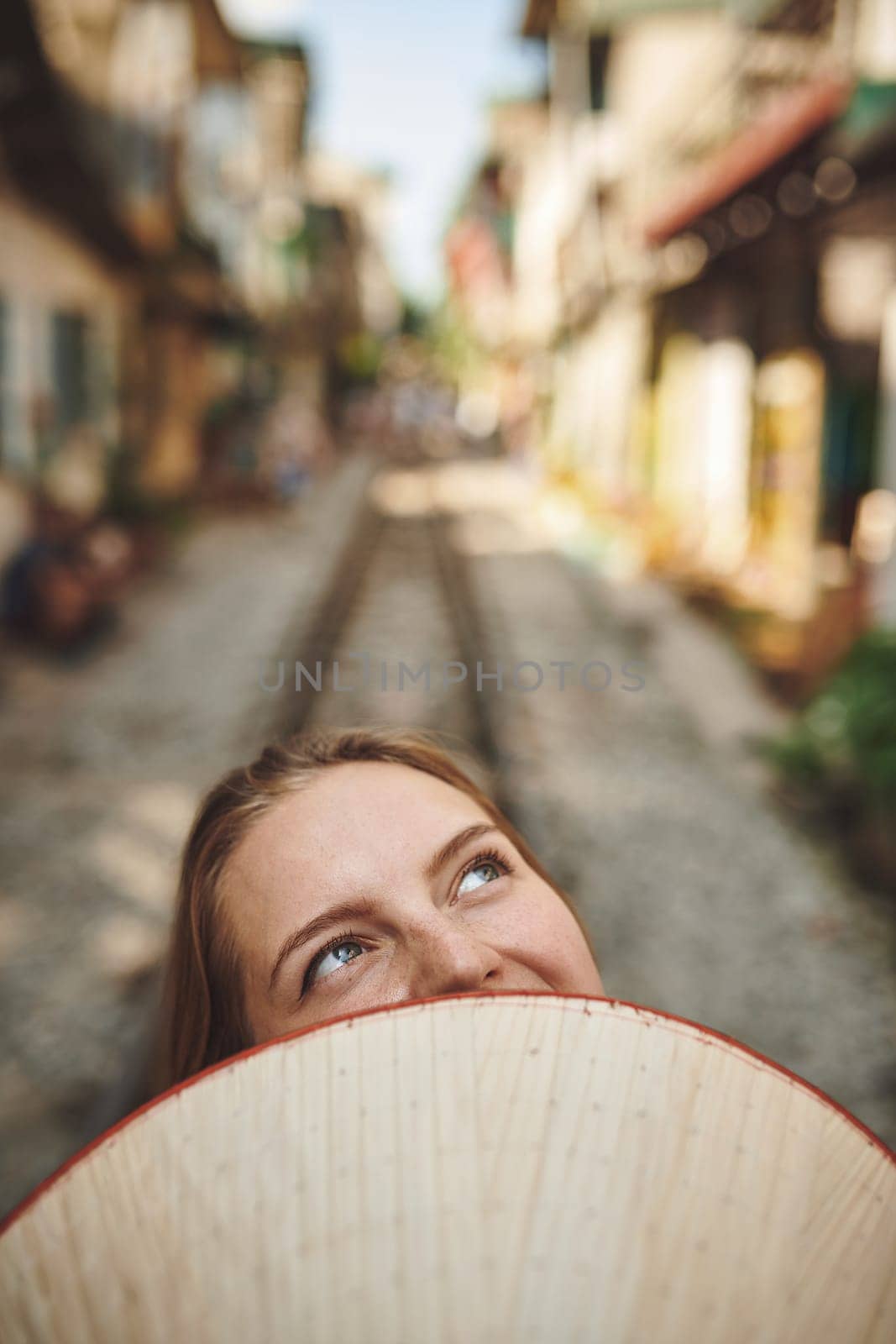 Travel means adventure. a woman holding a conical hat in front of her face. by YuriArcurs