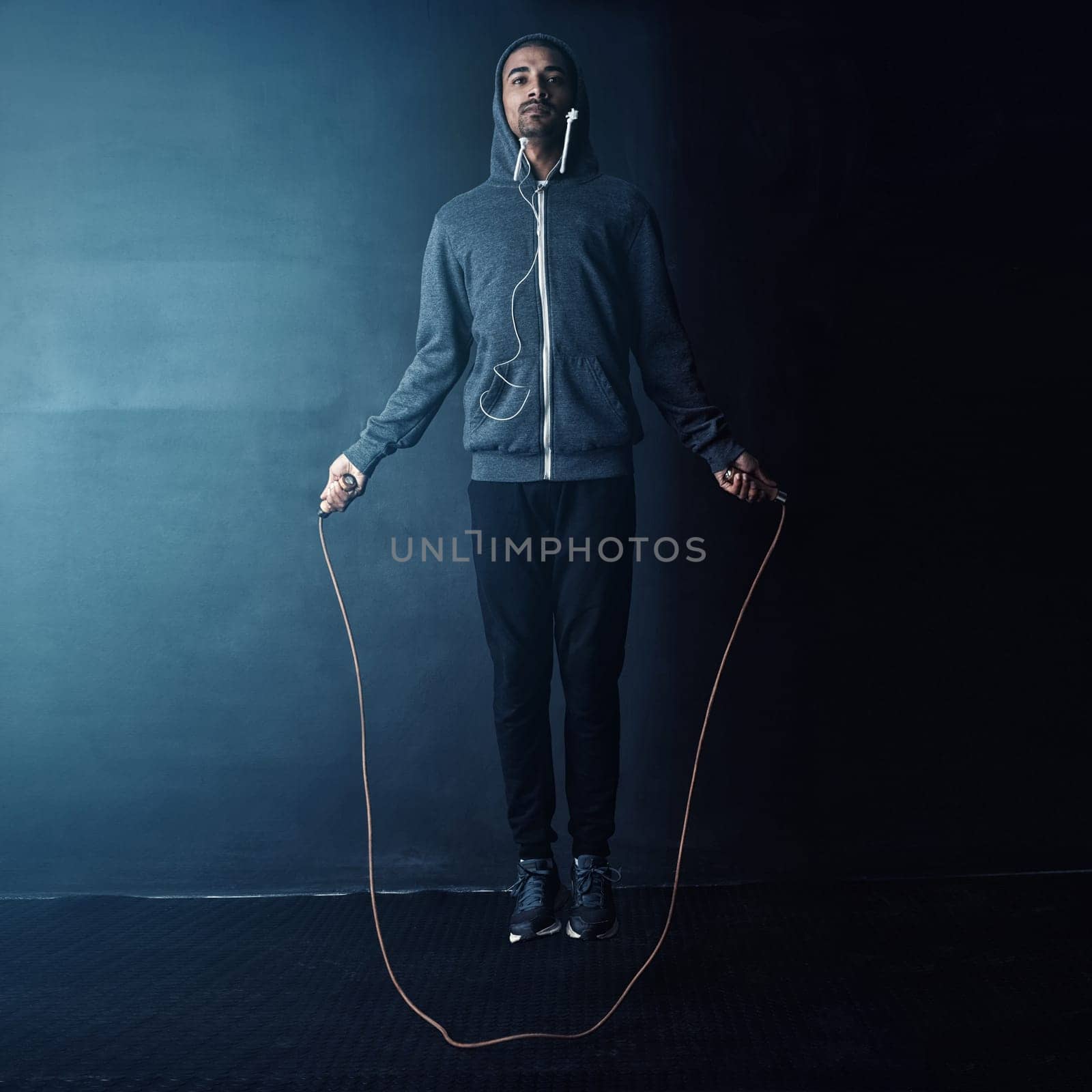 Skipping his way to fitness. Studio shot of a young man skipping against a dark background. by YuriArcurs