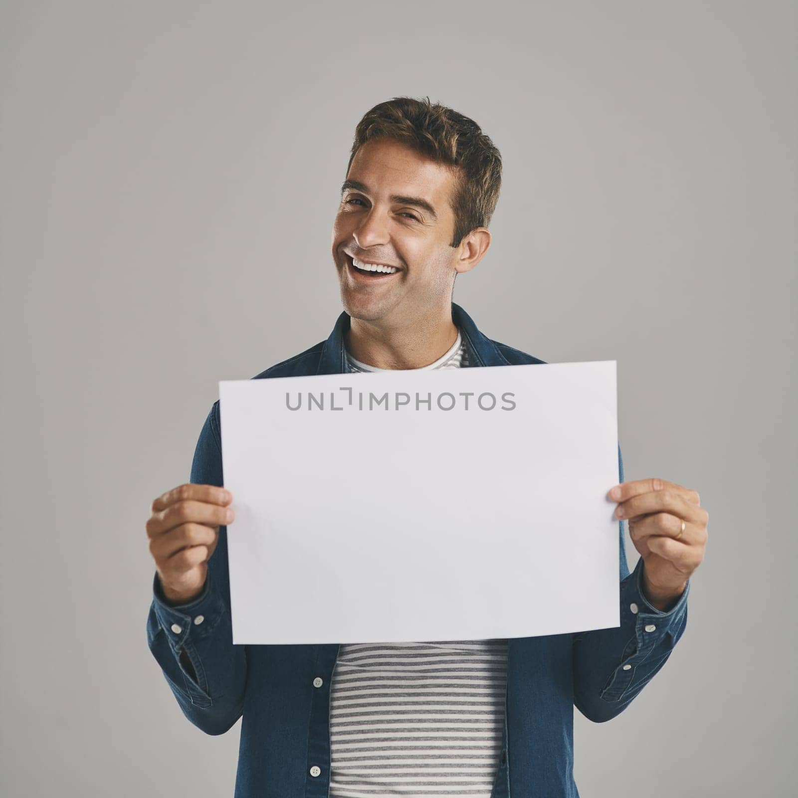 I have a very special message just for you. Studio portrait of a young man holding a blank placard against a grey background. by YuriArcurs