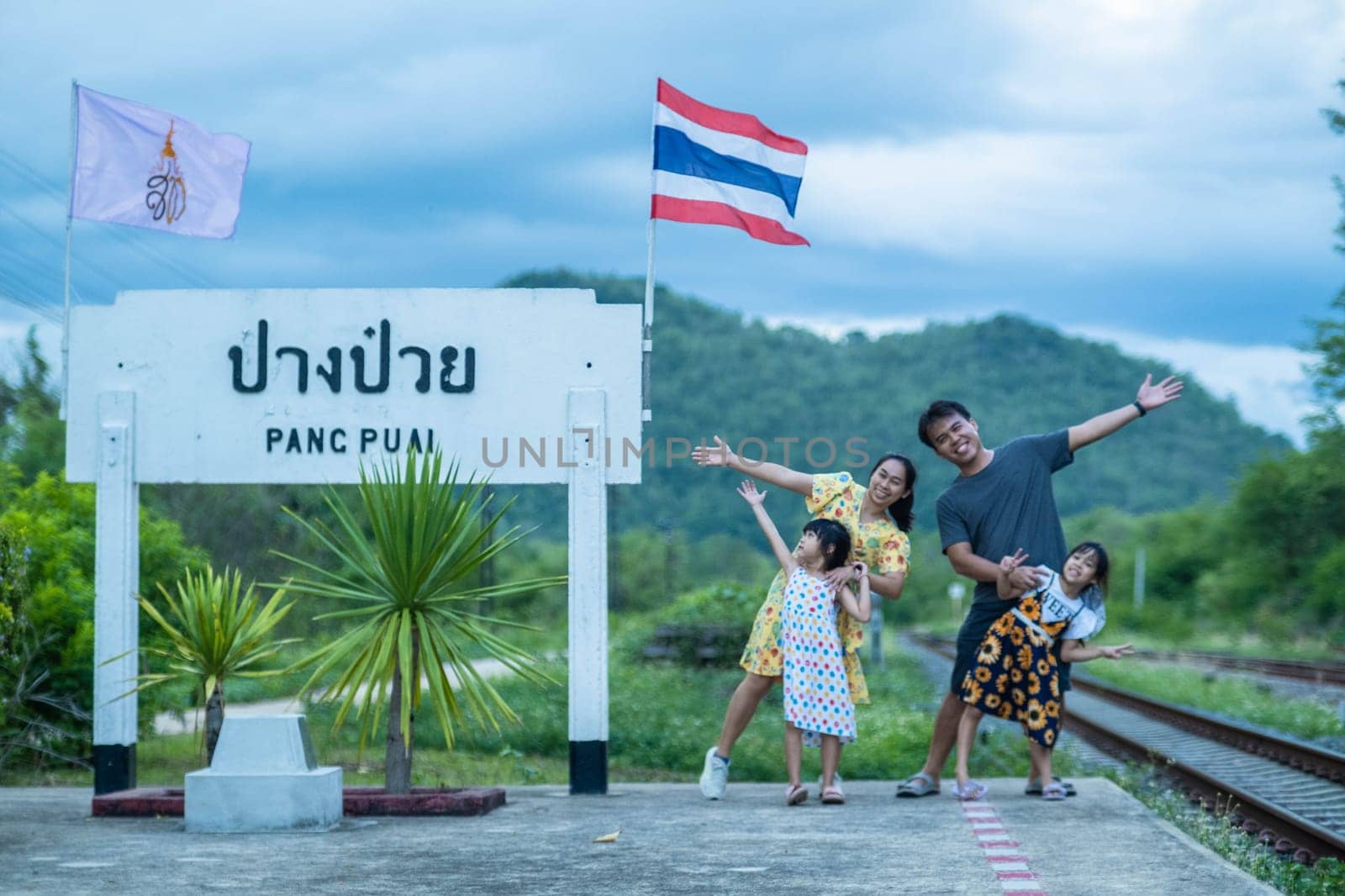 8 June 2023: Lampang, Thailand - Happy family taking pictures together at Pang Puai Railway Station against a background of green mountains and trees. by TEERASAK