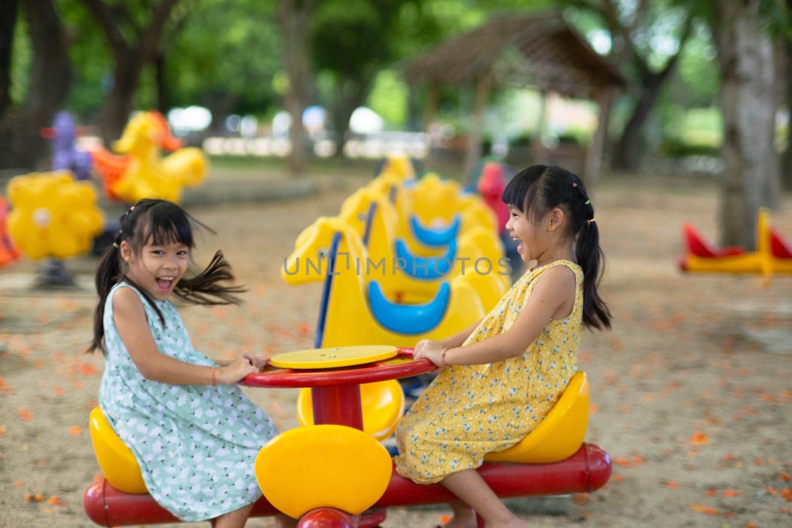 Children sit on a carousel in the playground together. Children playing at outdoor playground in the park on summer vacation. Healthy activity.
