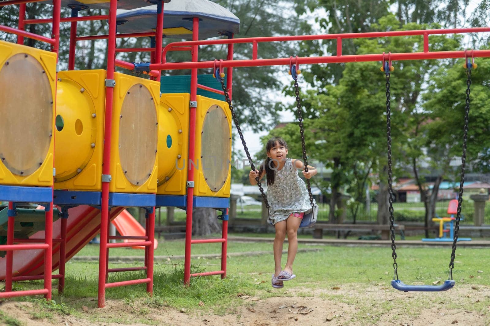 Happy girl having fun on the swing. Little Asian girl playing at outdoor playground in the park on summer vacation. Healthy activity.