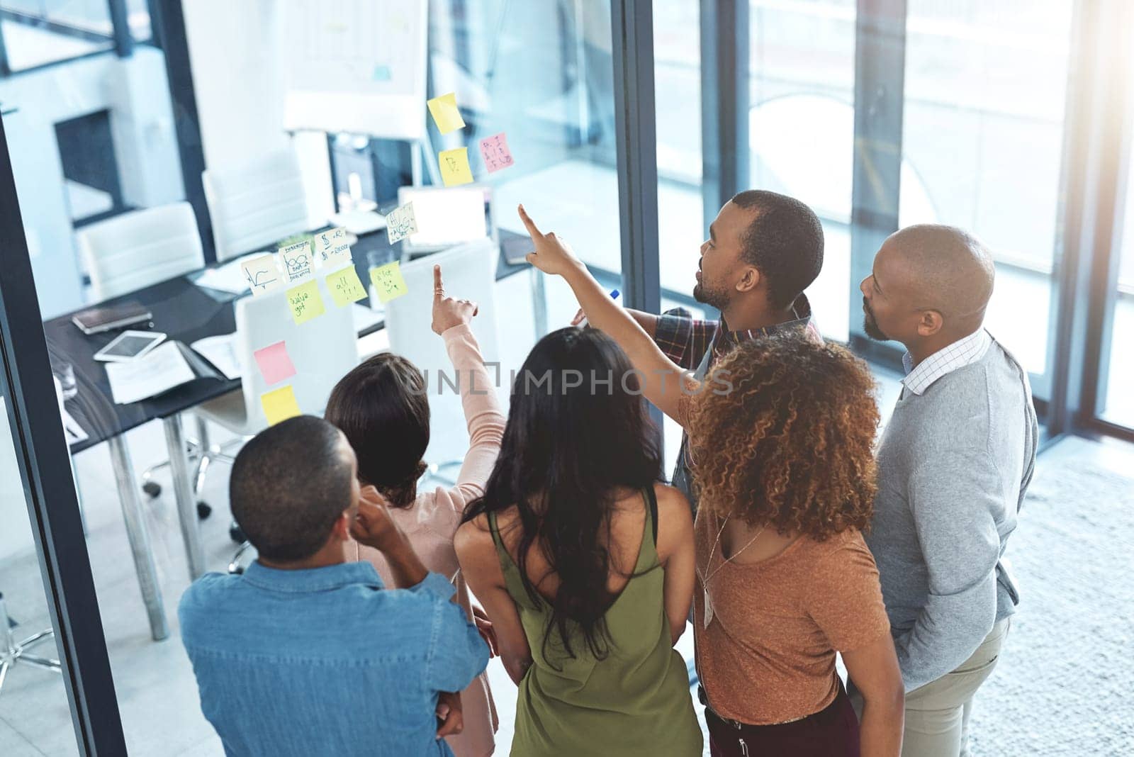 Asking the real questions. High angle shot of a group of coworkers brainstorming on a glass wall