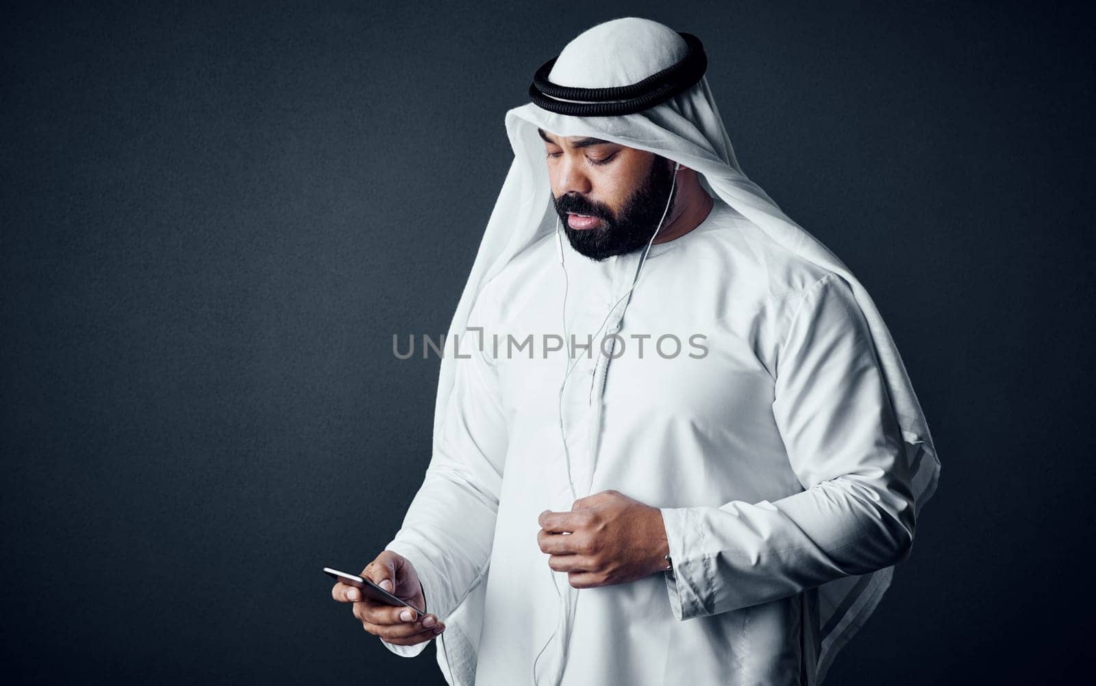 Upgrading his traditional ways. Studio shot of a young man dressed in Islamic traditional clothing posing against a dark background. by YuriArcurs