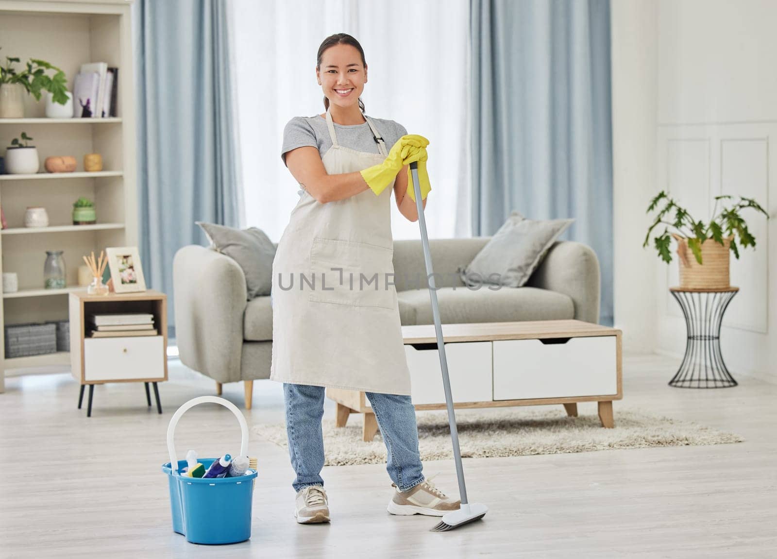 Portrait, broom and a woman cleaner sweeping the living room of a home for hygiene, service or housework. Smile, spring cleaning or housekeeping with an asian female maid standing in a domestic house.