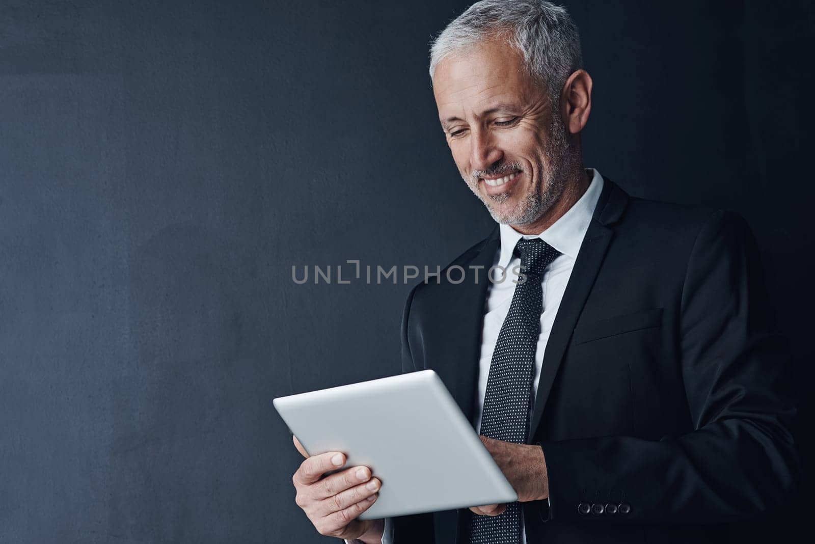 Smart technology is a staple for the business savvy. Studio shot of a mature businessman using a digital tablet against a dark background. by YuriArcurs