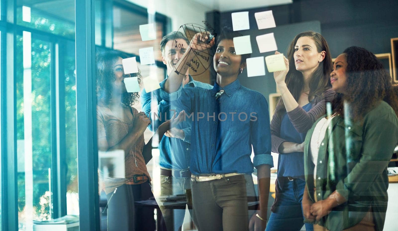 Looking through opportunities for growth and improvement. a group of businesspeople brainstorming with notes on a glass wall in an office. by YuriArcurs