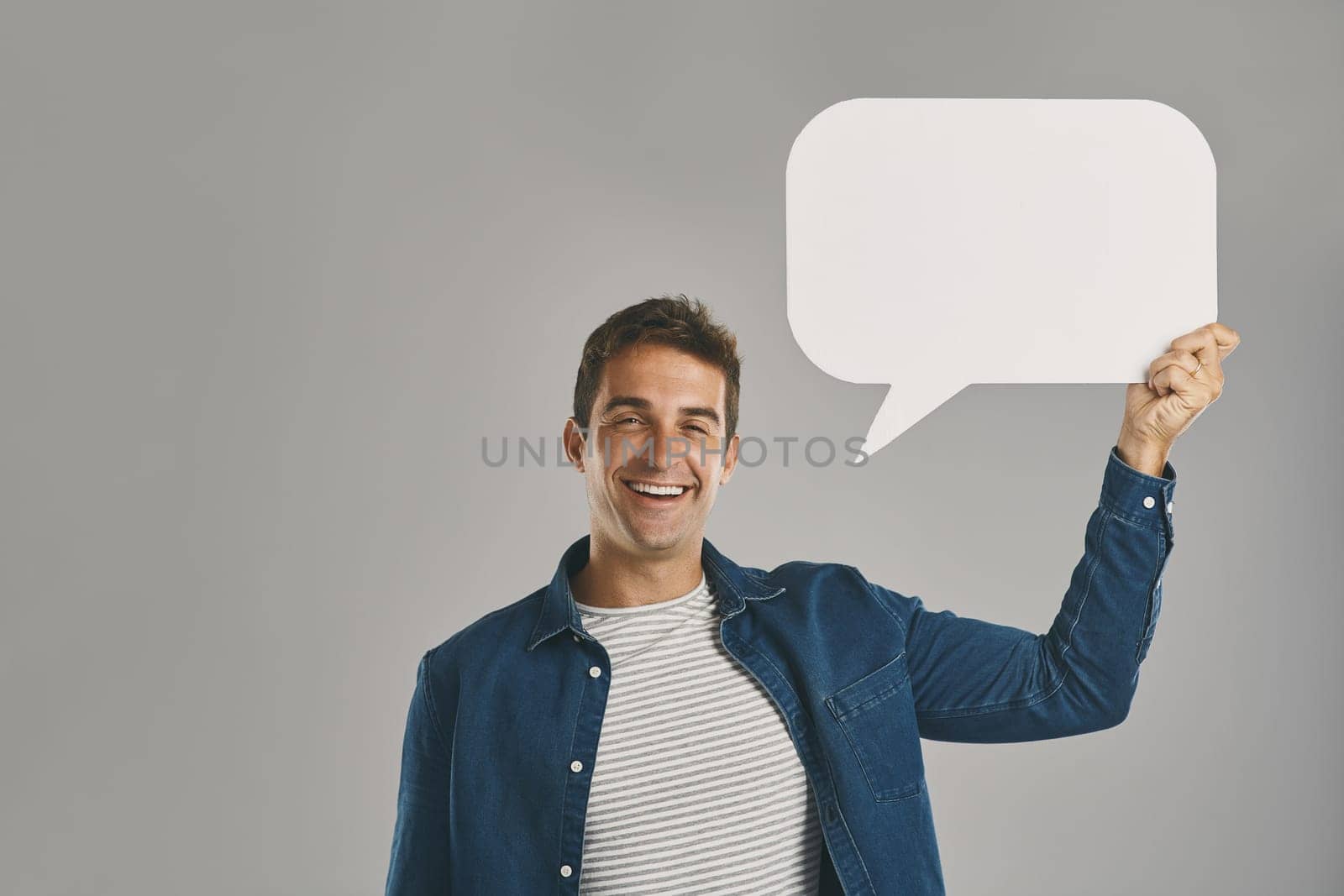 Speak your mind. Studio portrait of a young man holding a speech bubble against a grey background. by YuriArcurs