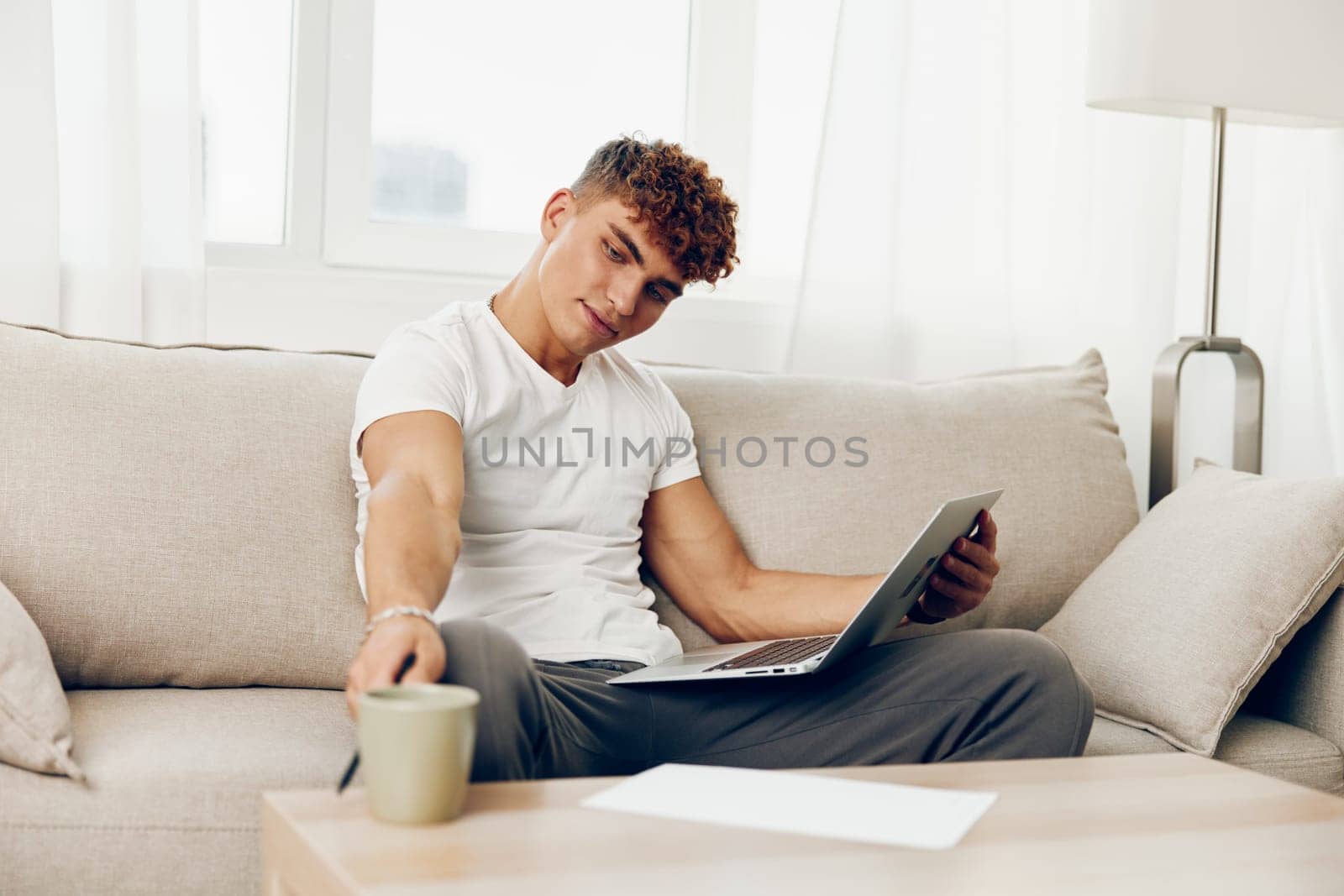 man interior sitting computer blissful browsing sofa home room call curly indoor happy phone lifestyle using person laptop notebook looking male chat