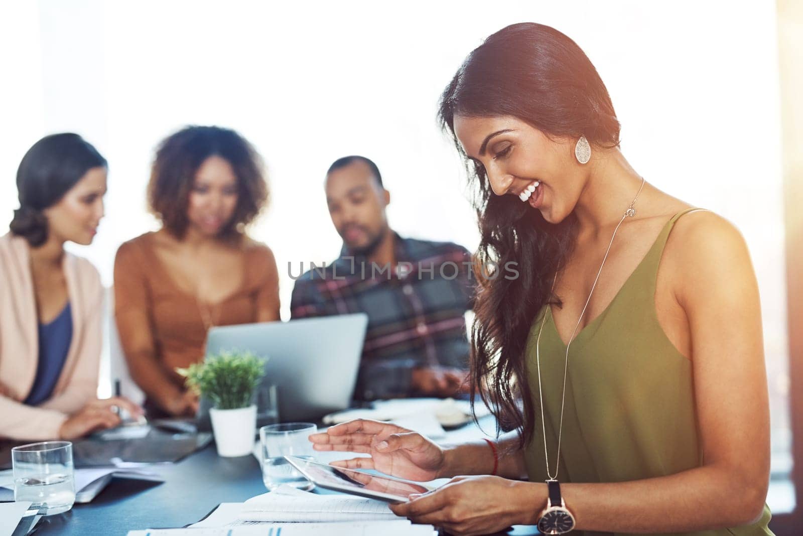 Smart technology makes meetings a breeze. a young woman using a digital tablet during a meeting with her colleagues in the background. by YuriArcurs