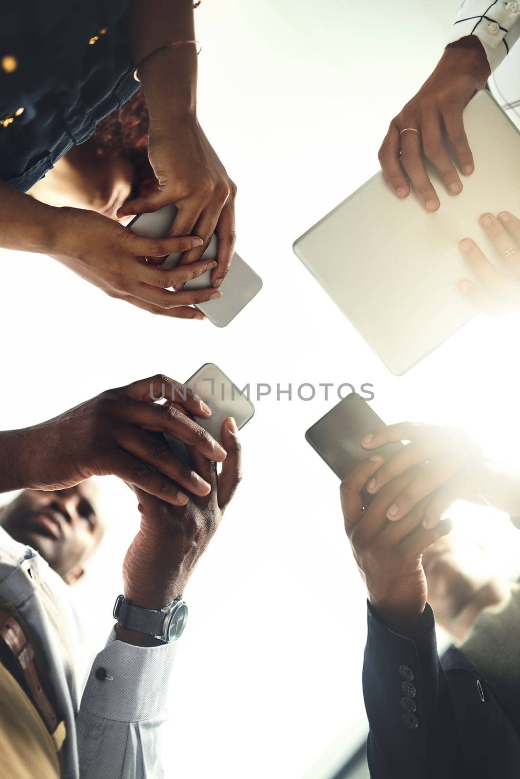 Sharing and storing business updates through the cloud. Closeup shot of a group of businesspeople using their digital devices in synchronicity in an office. by YuriArcurs
