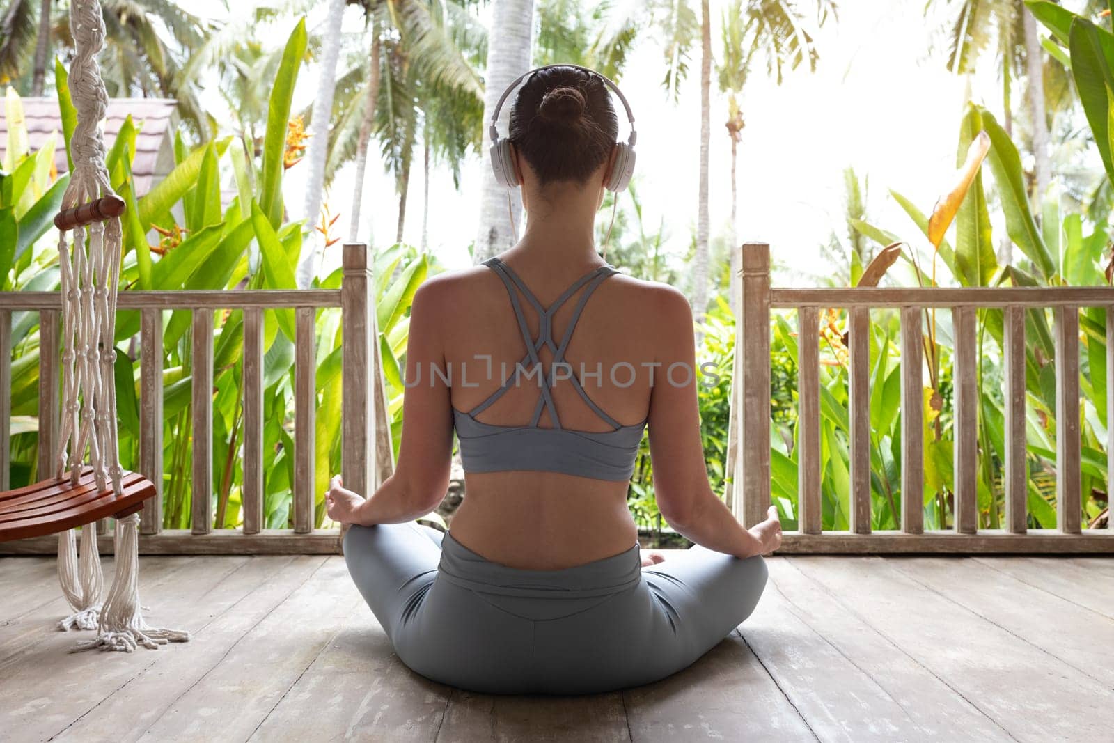 Rear view image of young woman meditating in nature using headphones. Healthy lifestyle and technology concept.