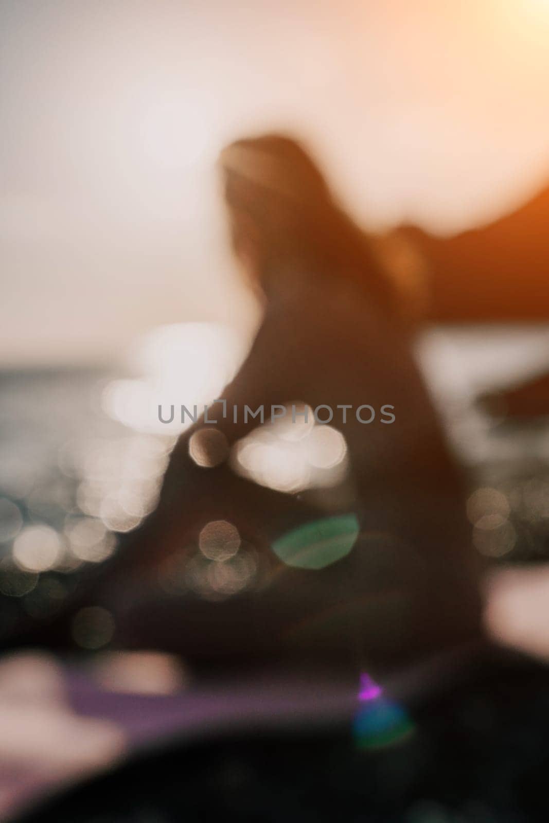 Abstract defocused silhoute of middle aged well looking woman with black hair doing Pilates with the ring on the yoga mat near the sea on the pebble beach. Female fitness yoga concept. by panophotograph