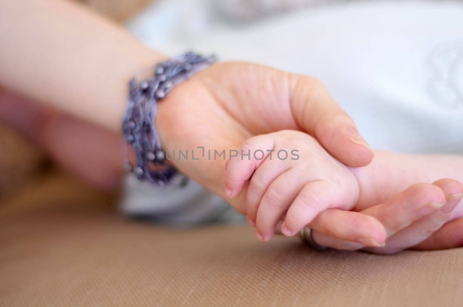 Love, family and mother holding hands with her baby in the home for trust, care or bonding together closeup. Children, hand or comfort with a mama and newborn infant in a house to nurture growth by YuriArcurs