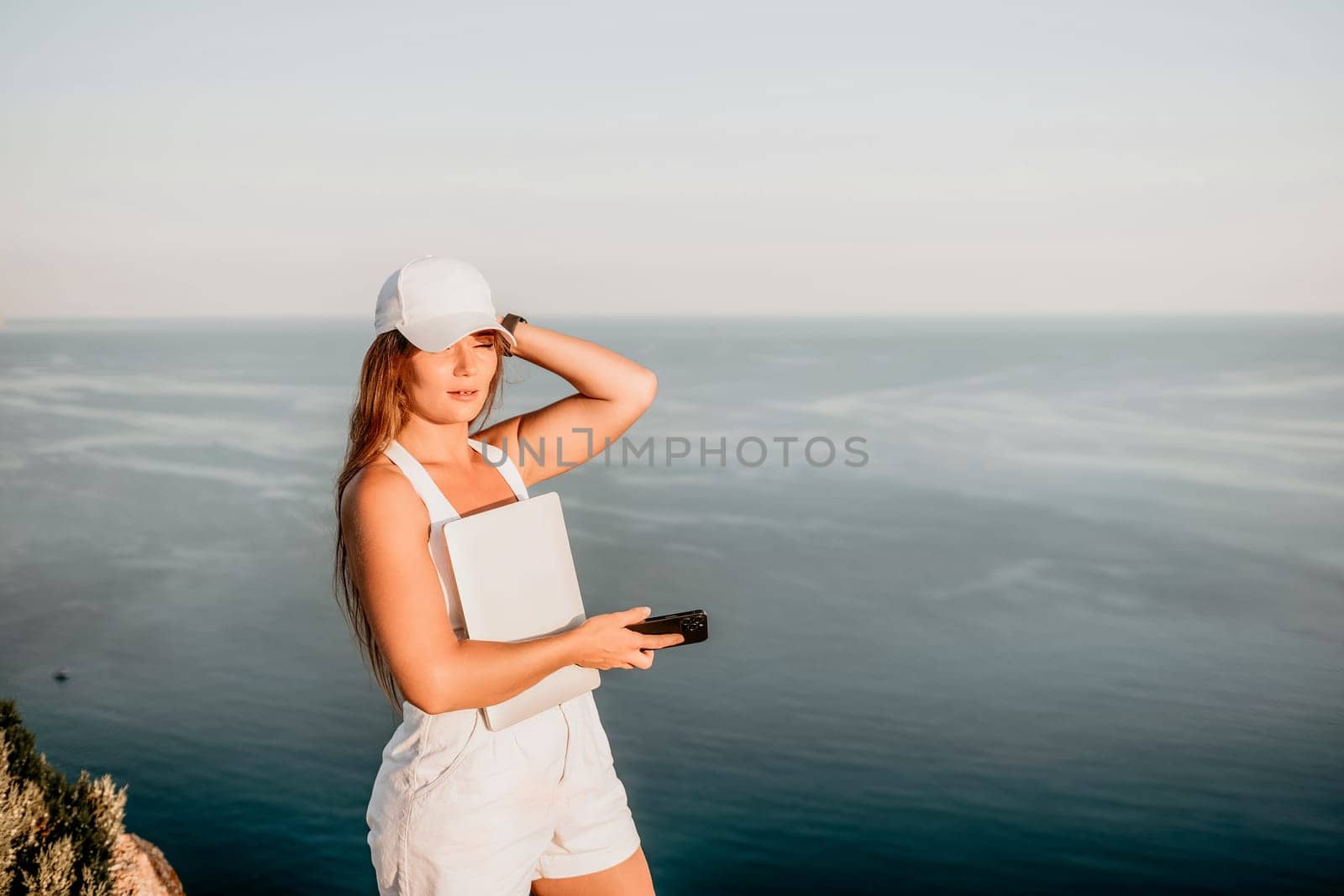 Woman laptop sea. Working remotely on seashore. Happy successful woman female freelancer in straw hat working on laptop by the sea at sunset. Freelance, remote work on vacation by panophotograph