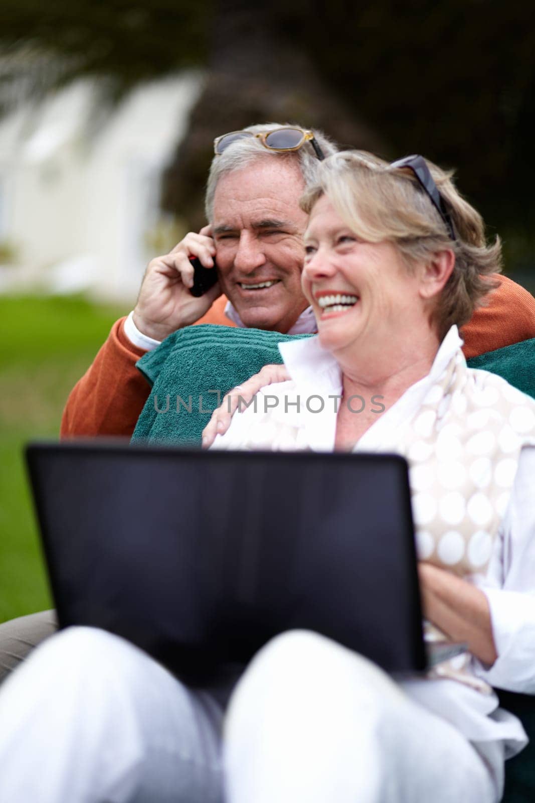 Phone call, laptop and an old couple in the garden of a hotel for travel or vacation at a luxury resort. Love, technology or communication with a senior man and woman tourist outdoor at a lodge by YuriArcurs