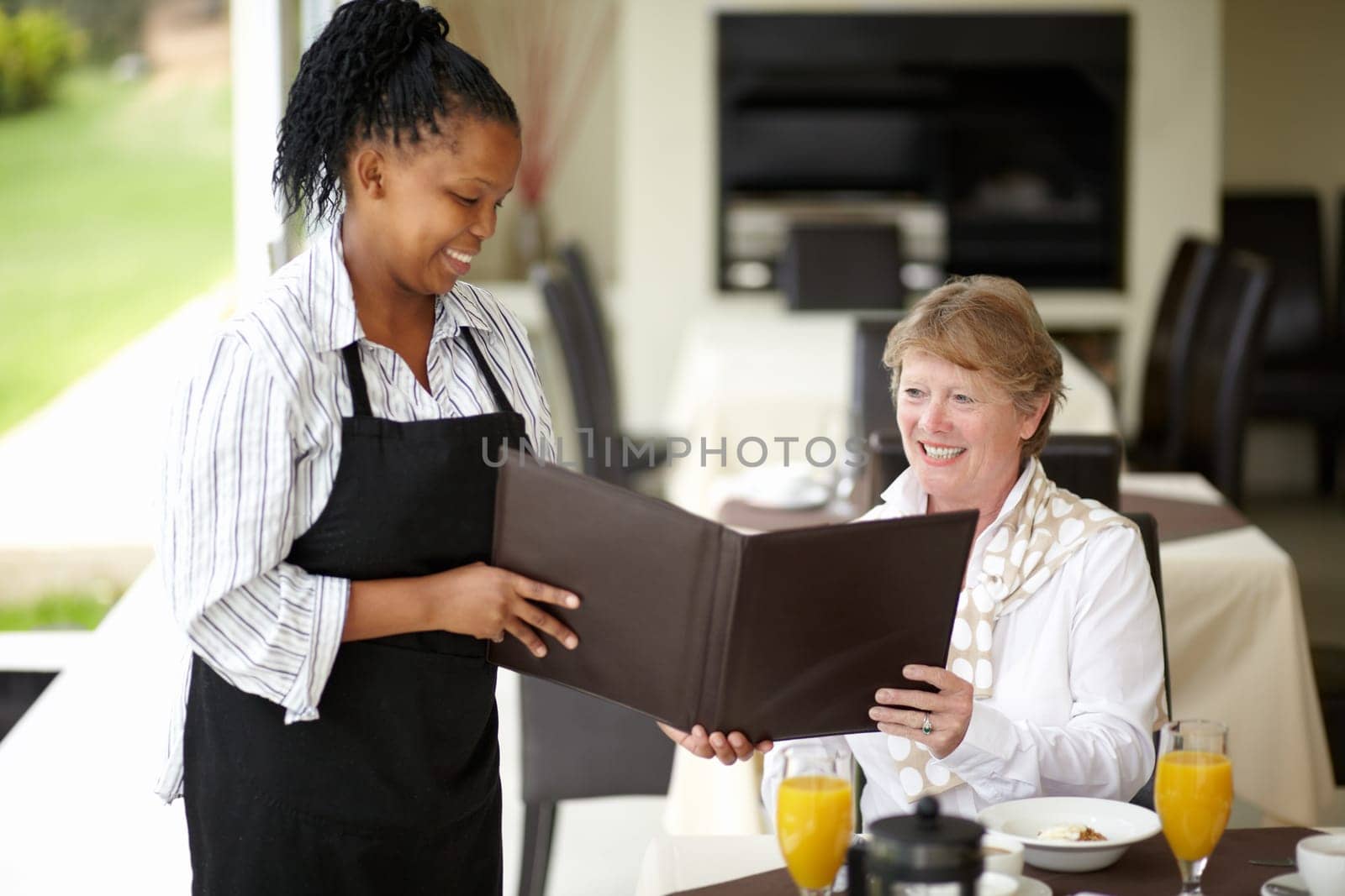 Waitress, service and senior woman in a restaurant for breakfast or lunch at a hotel with a menu and choice of food. Friendly, order and elderly person happy on vacation or holiday for hospitality by YuriArcurs