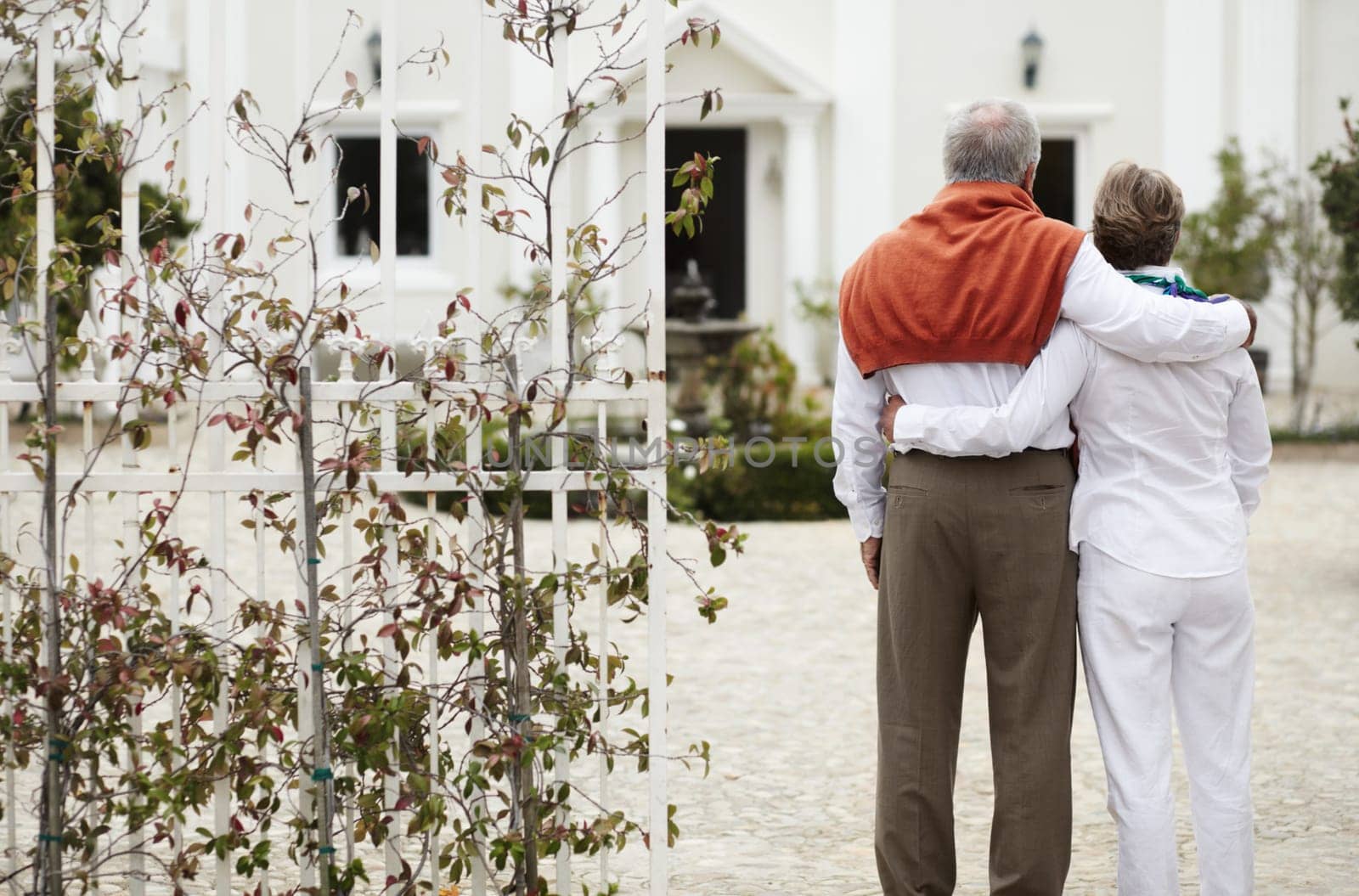 Back, hug and a senior couple at a hotel for a holiday, retirement travel and love together. Affection, nature and an elderly man and woman on a vacation at a resort or manor and hugging at the gate.