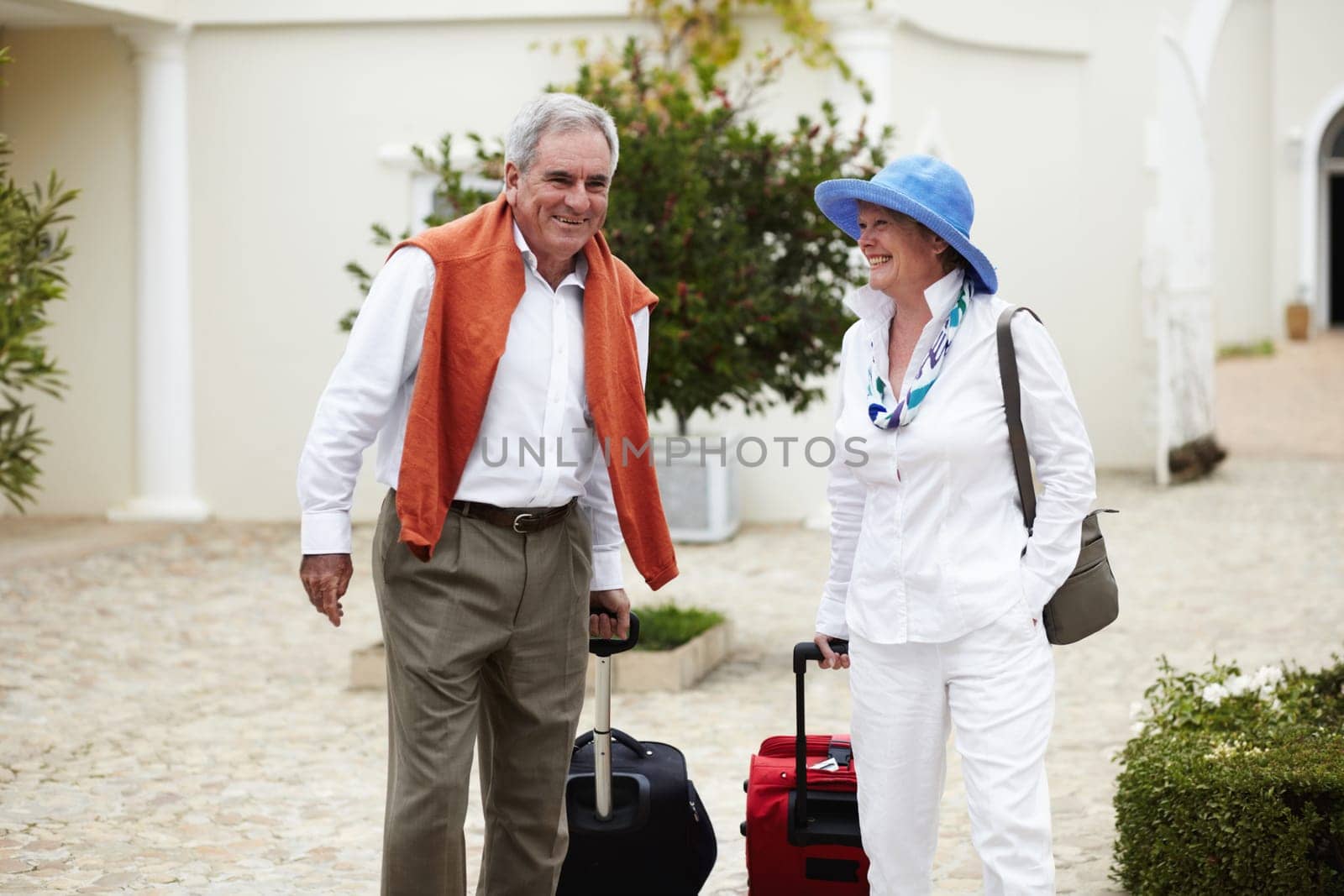 Travel, vacation and senior couple walking with suitcase in a holiday location happy in retirement together by a hotel. Bag, smile and elderly people on a journey or man and woman walk in happiness by YuriArcurs