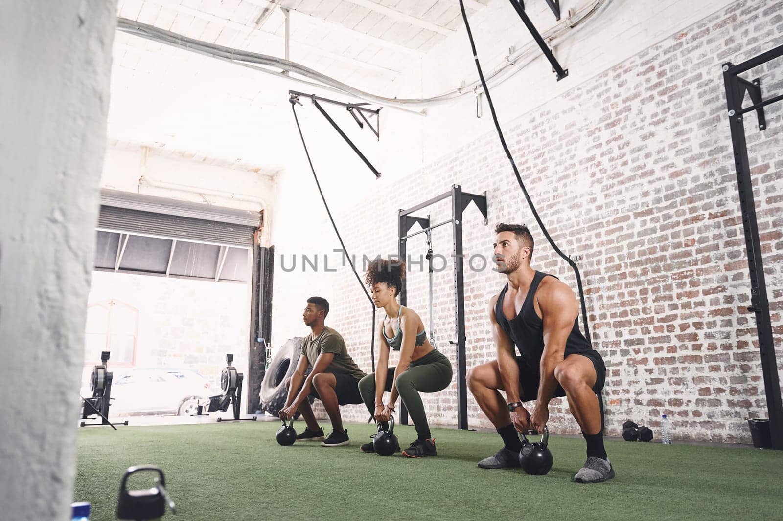 Focus on every single rep. a fitness group holding kettlebells while doing squats at the gym. by YuriArcurs