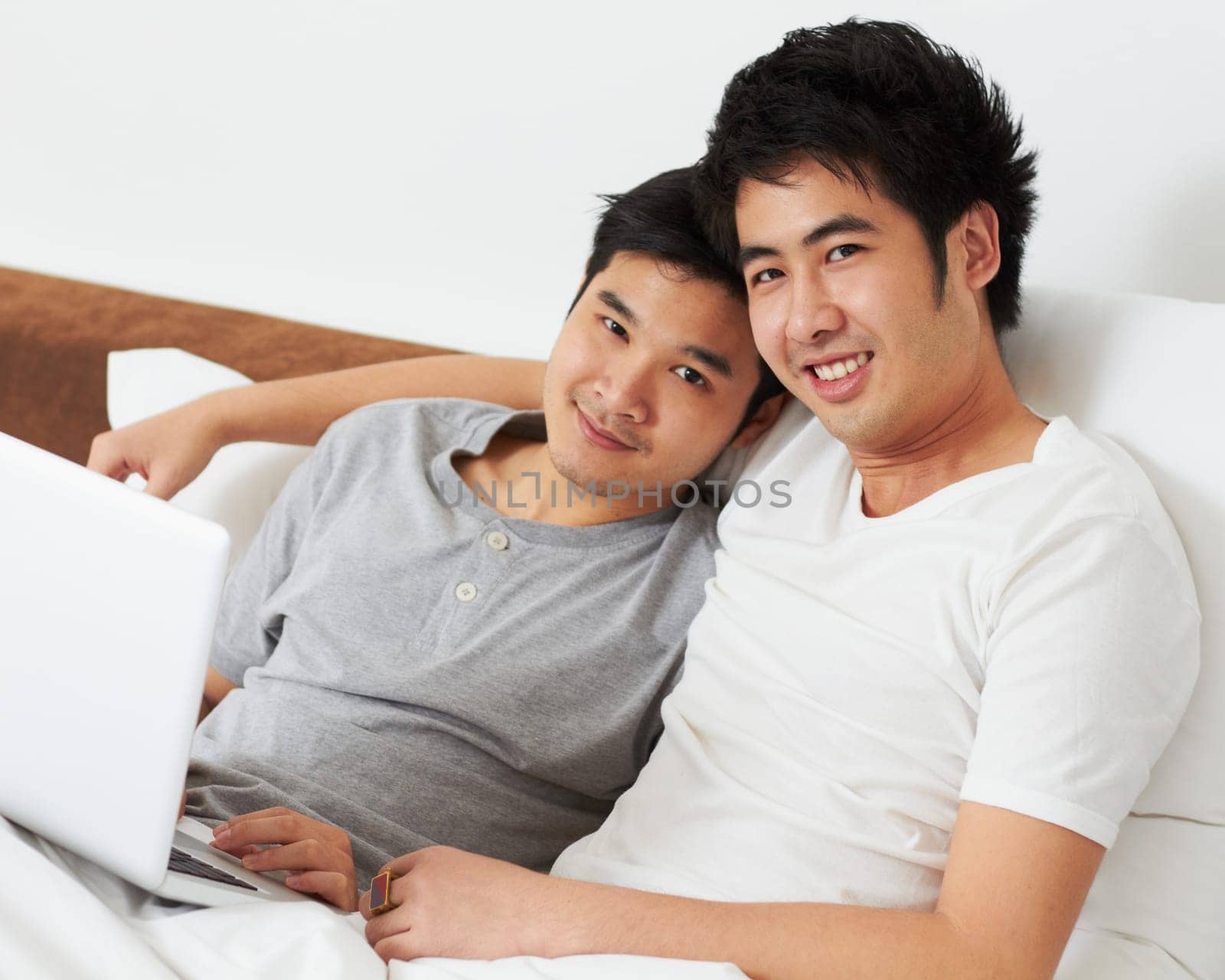 Portrait, laptop and bed with a gay couple watching a movie together while bonding in the morning. Love, happy or smile with an lgbt man and partner lying in their bedroom to relax while streaming.