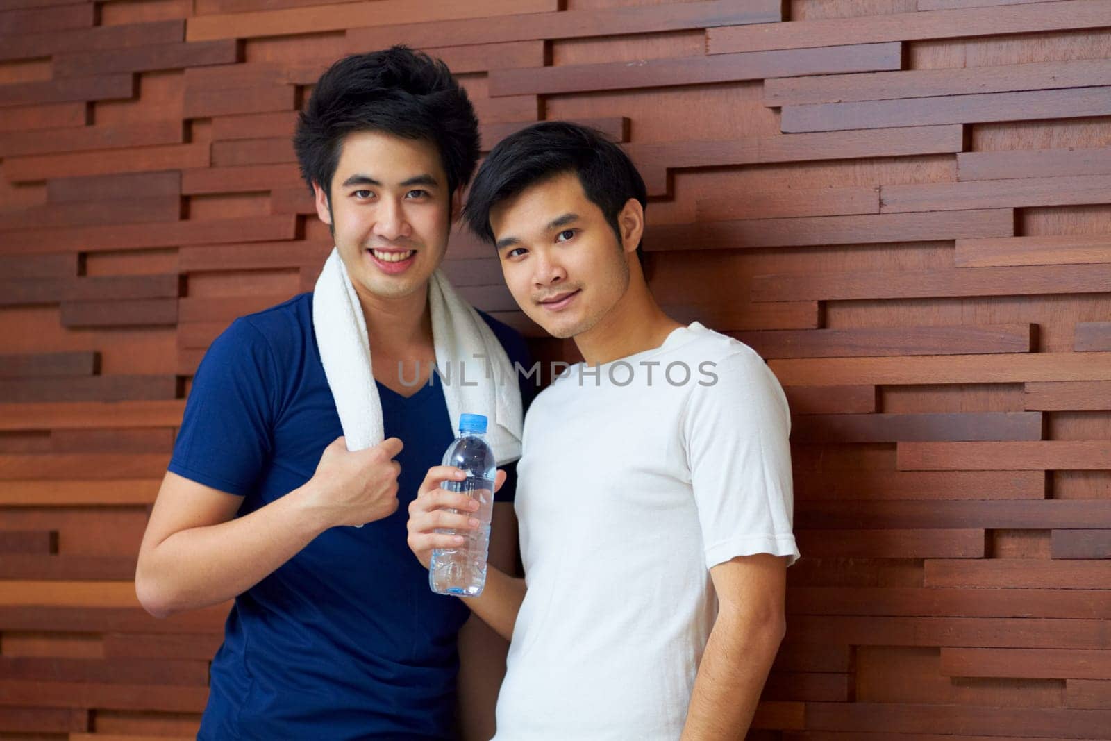 Happy, portrait and gay couple at the gym with water on a break from a workout together. Smile, wellness and Asian lgbt men training at a club for exercise, health and happiness with fitness.