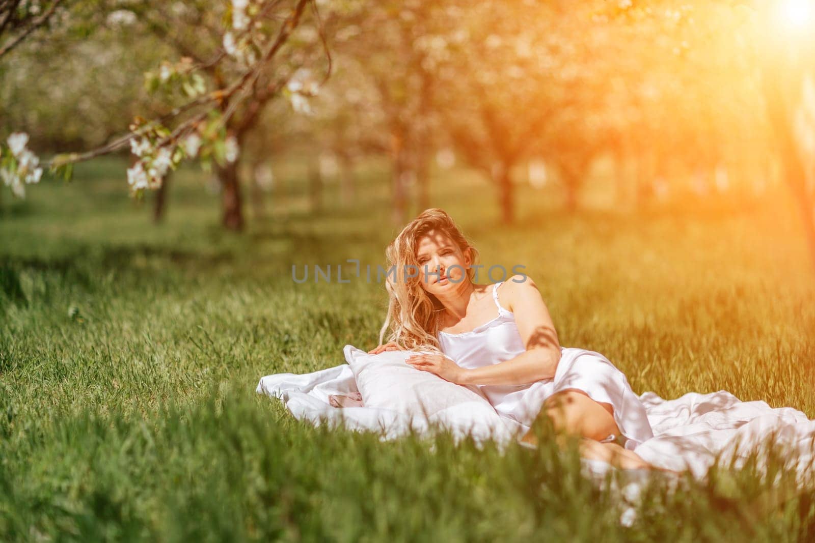 woman garden. she sleeps on a white bed in the fresh spring grass in the garden. Dressed in a blue nightgown