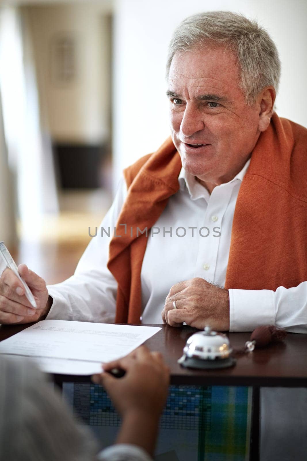 Hotel, reception and an old man signing documents for check in at a luxury hospitality resort for vacation. Paper, signature and travel with a happy senior male tourist in a lodge for holiday travel.
