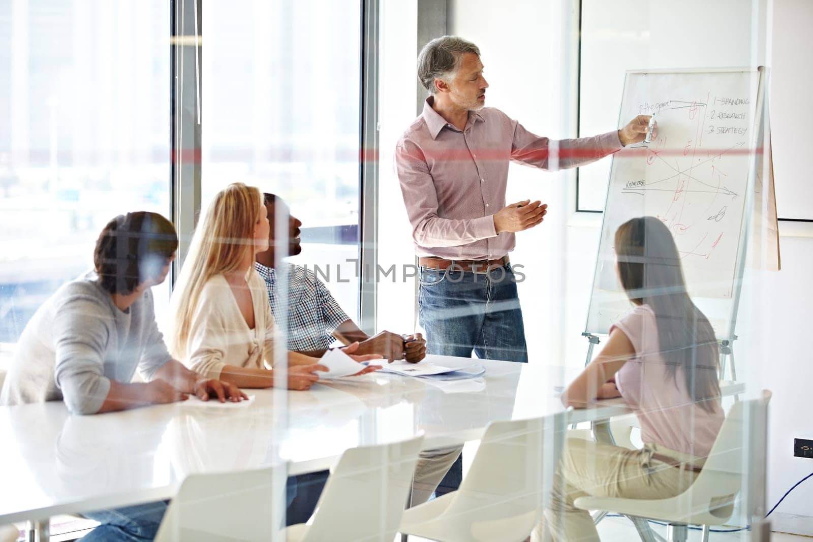 Planning, mature mentor with colleagues and chart in a boardroom of their modern workplace. Teamwork or collaboration, data review or brainstorming and coworkers working together in business meeting by YuriArcurs