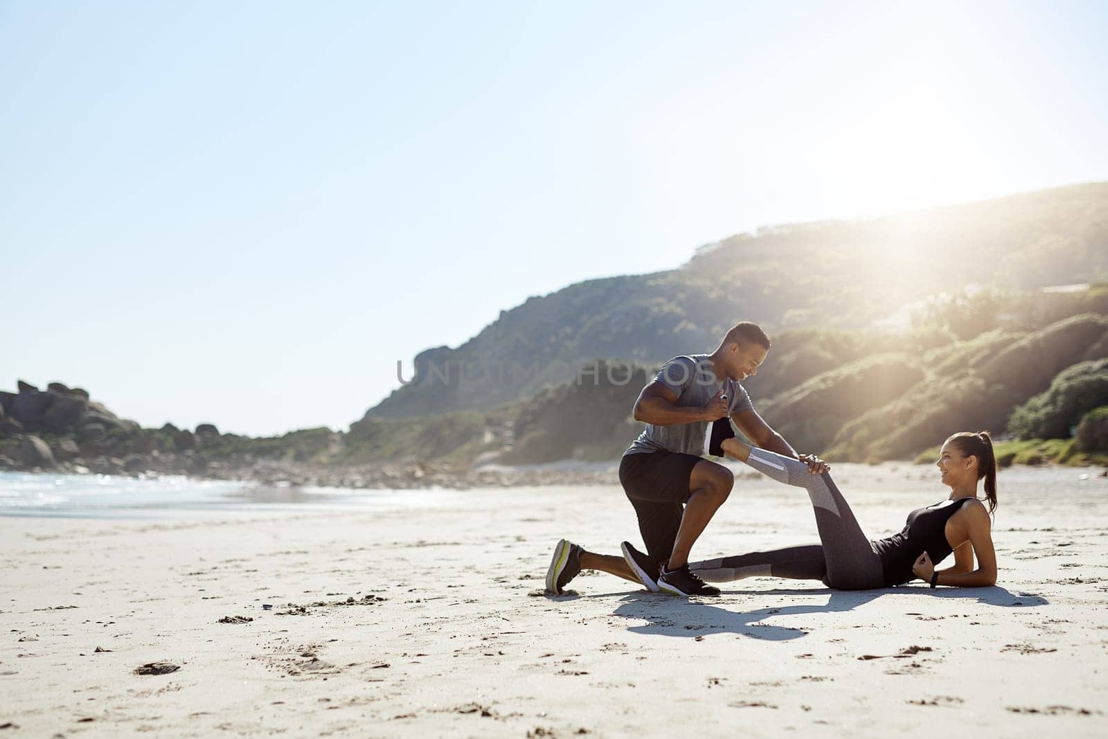 Preparing their bodies for a full workout. a sporty young couple stretching while exercising along the beach