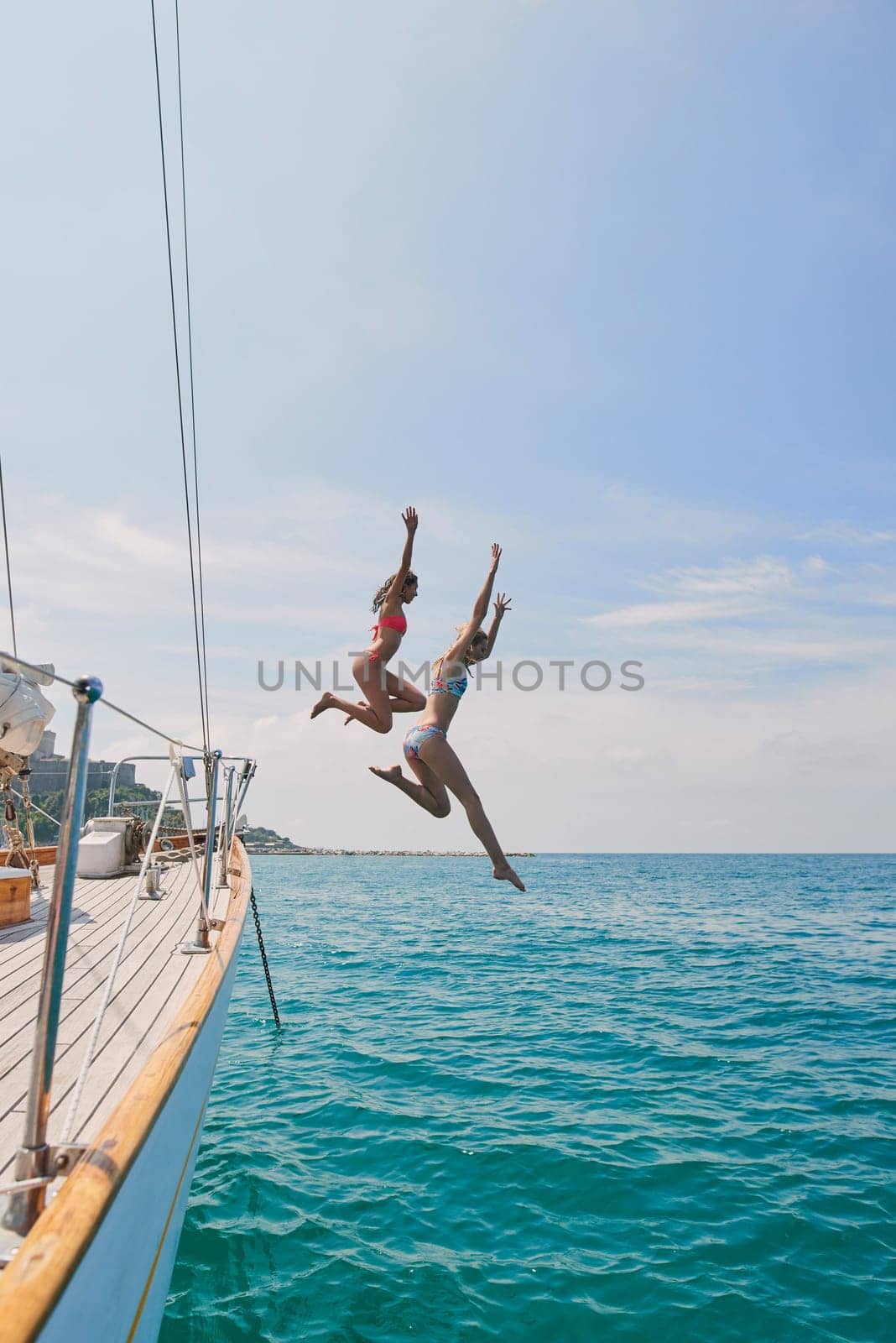 Summer, sailing and friends jumping off a yacht together into the ocean for freedom, fun or swimming. Travel, energy and bikini with girls leaving a boat to jump into the sea while on a luxury cruise.