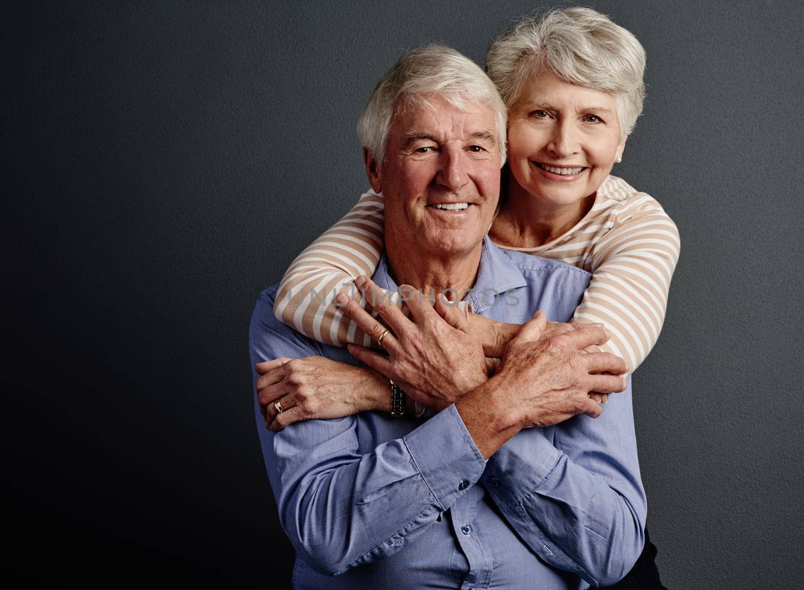 Ill never let him go. Studio portrait of an affectionate senior couple posing against a grey background. by YuriArcurs