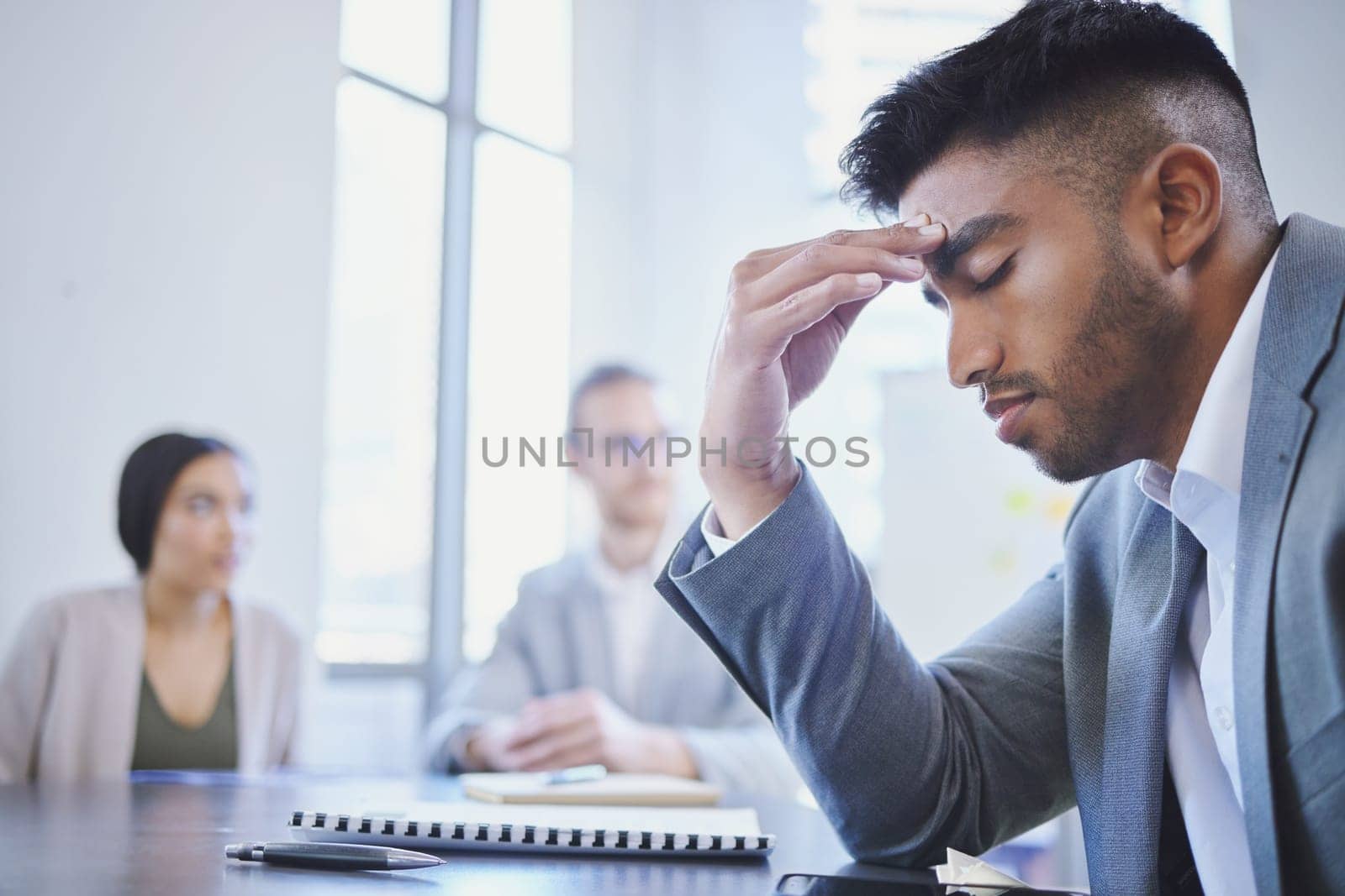 Mental health, businessman with a headache and at a business meeting with colleagues in a boardroom office at their workplace. Stress or depression, anxiety or tired and sad male person at a desk by YuriArcurs