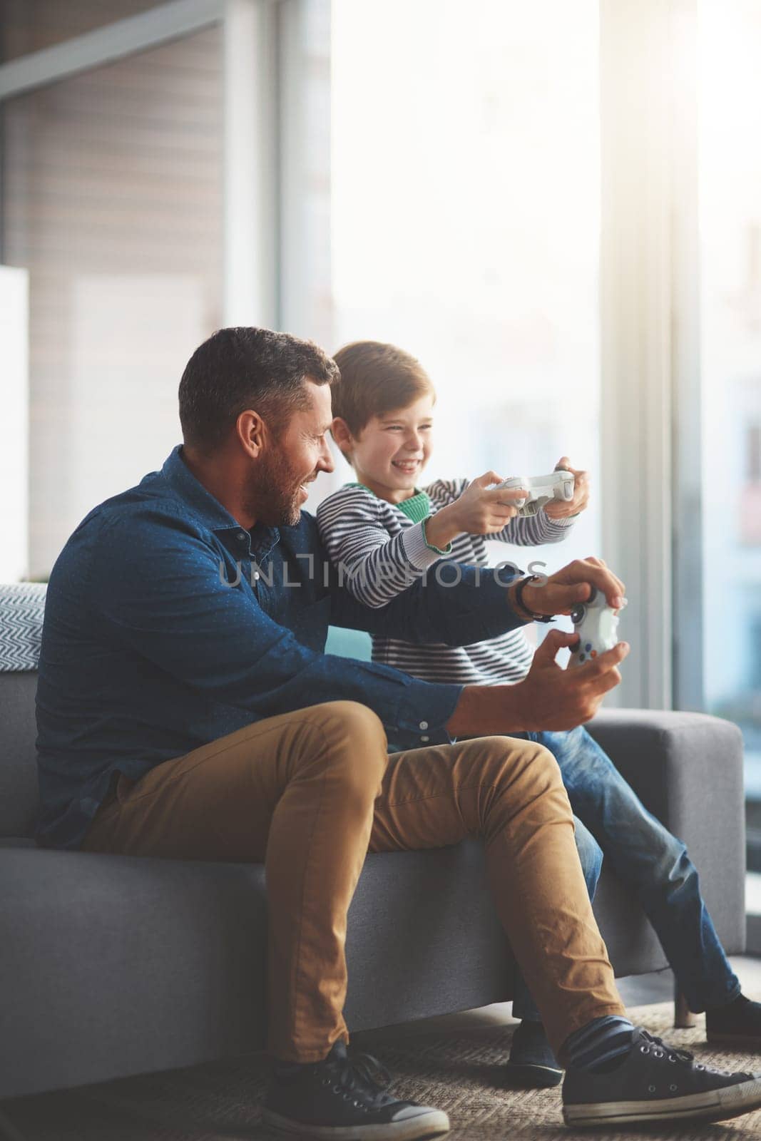 This is our most favorite game. a cheerful little boy and his father playing video games together on the television while being seated on the sofa at home during the day