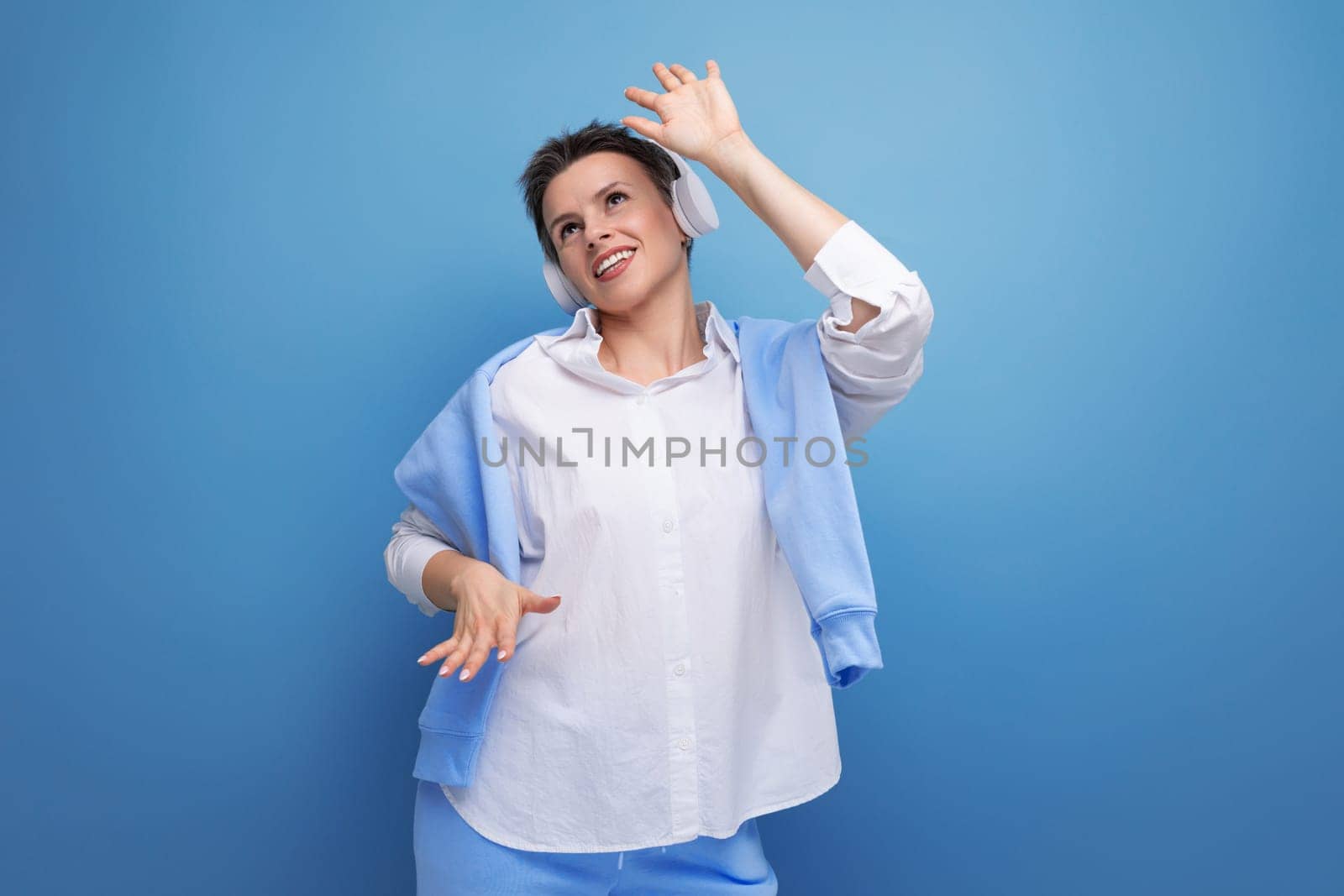 stylish young woman with short haircut enjoying music in headphones on studio background with copy space.