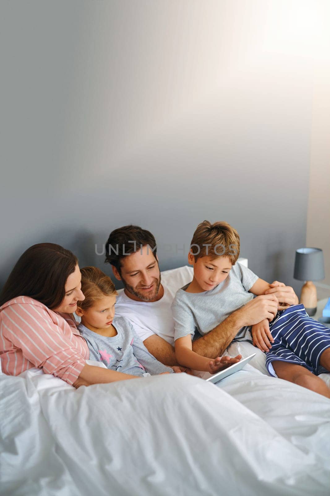 Weekends are for wifi in our home. a young family using a tablet while chilling in bed together at home. by YuriArcurs