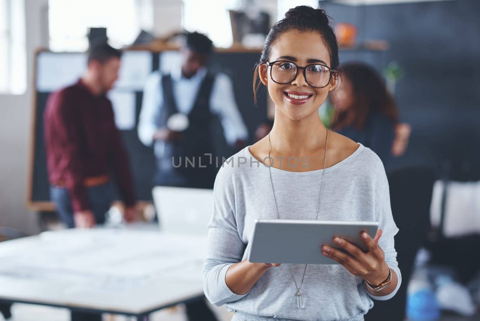 This tablet makes designing easy. Cropped portrait of an attractive young businesswoman using a tablet in the office with her colleagues in the background. by YuriArcurs