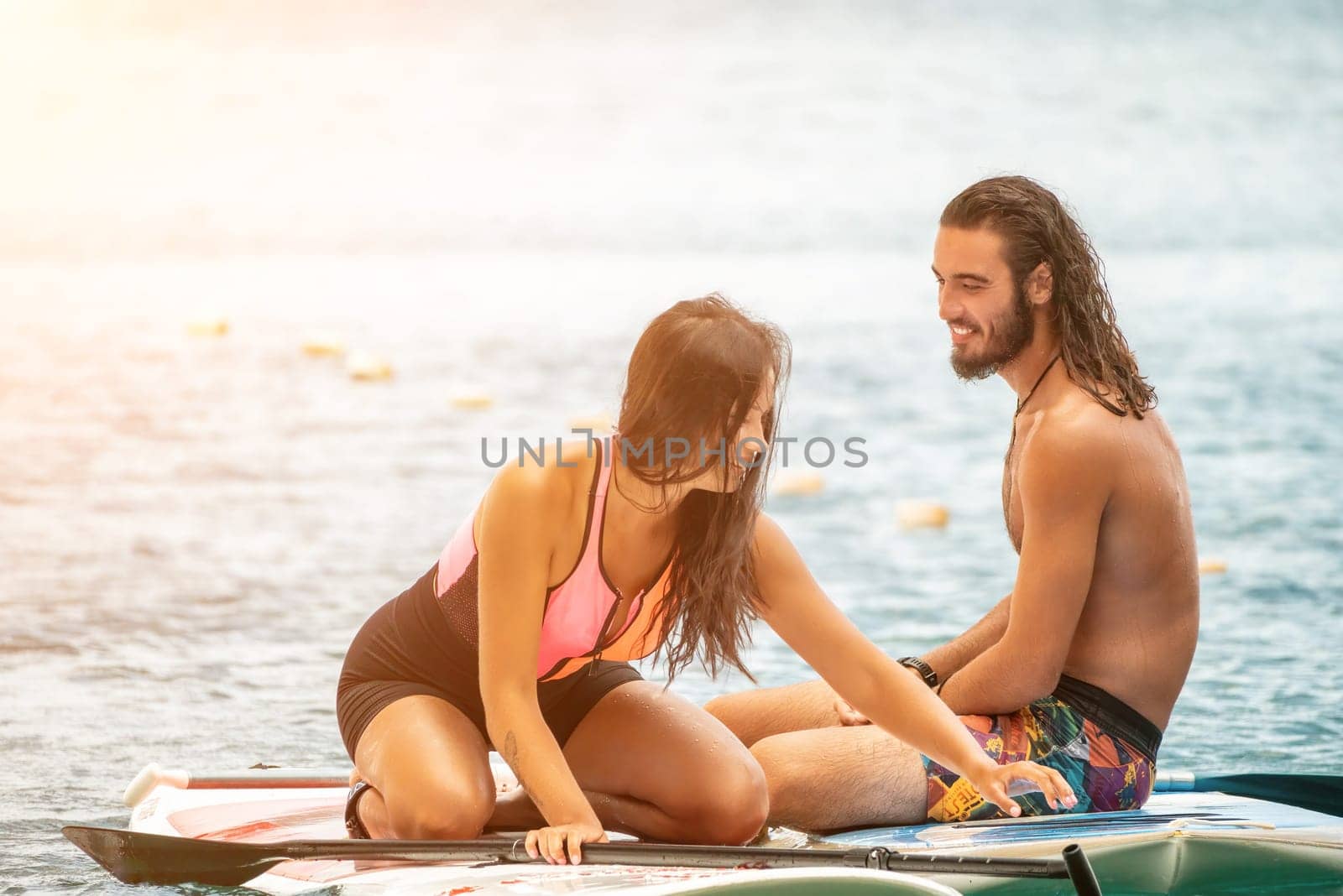 Sea woman and man on sup. Silhouette of happy young woman and man, surfing on SUP board, confident paddling through water surface. Idyllic sunset. Active lifestyle at sea or river