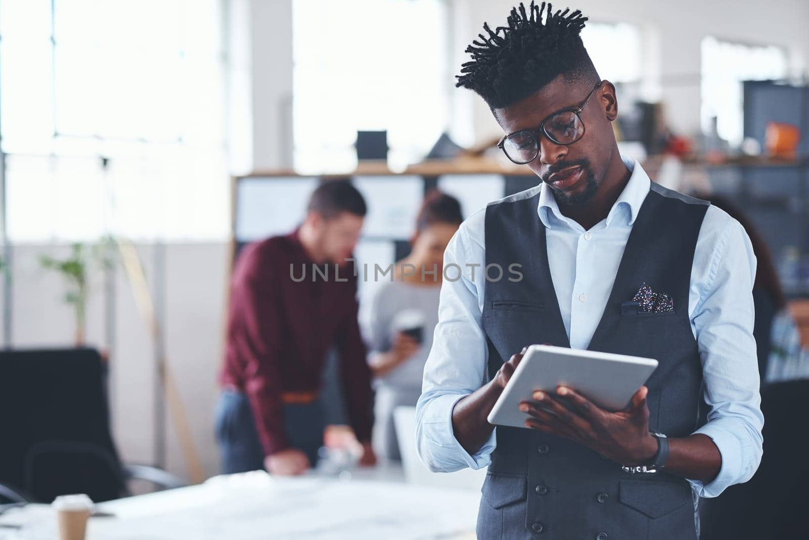 Just adding those final touches before the meeting. a handsome young businessman using a tablet in the office with his colleagues in the background