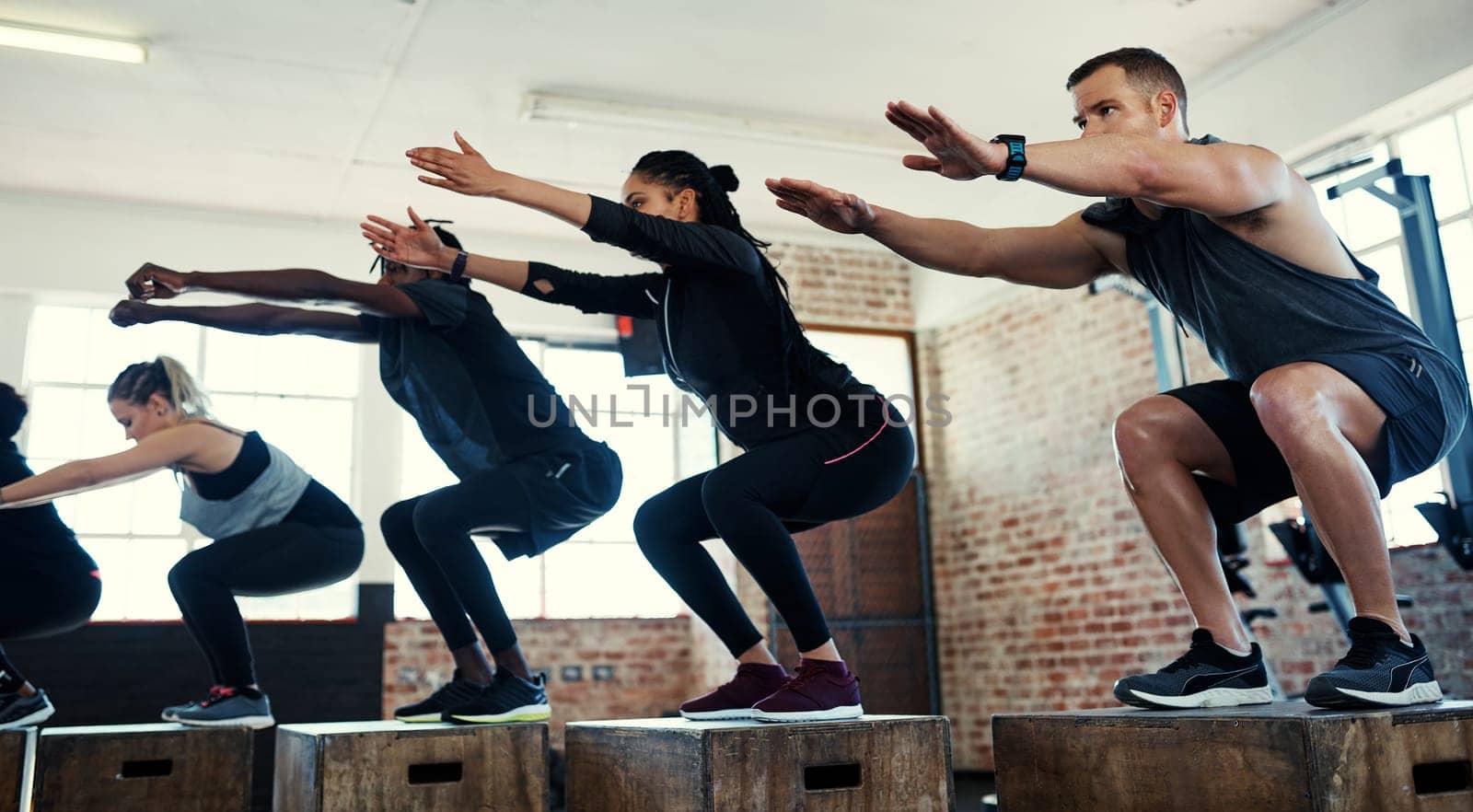 Working the legs. a focused group of young people doing lunges on crates as exercise inside of a gym. by YuriArcurs