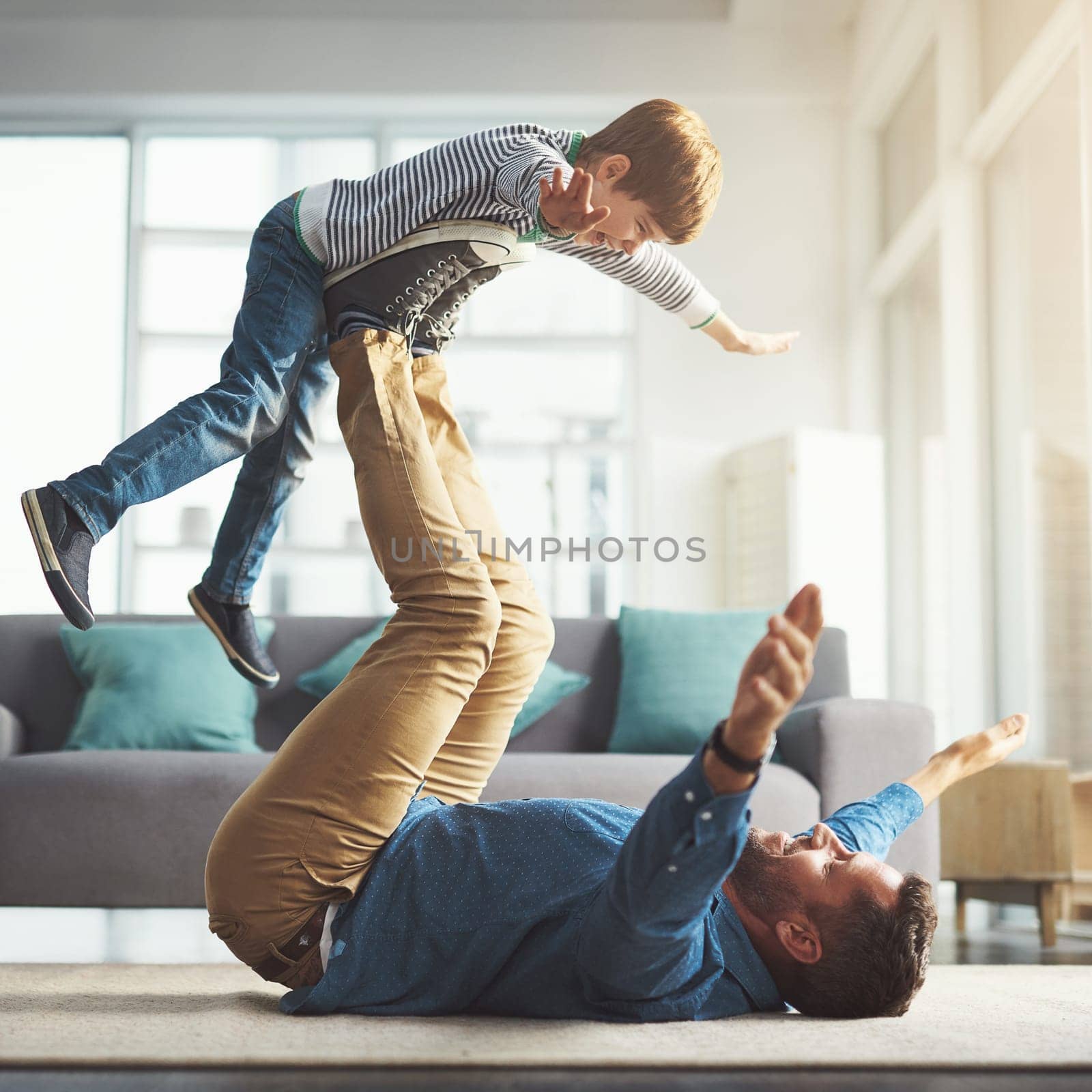 Raising up higher and higher. a cheerful little boy playing around and being lifted by his dad with his legs in the living room at home during the day