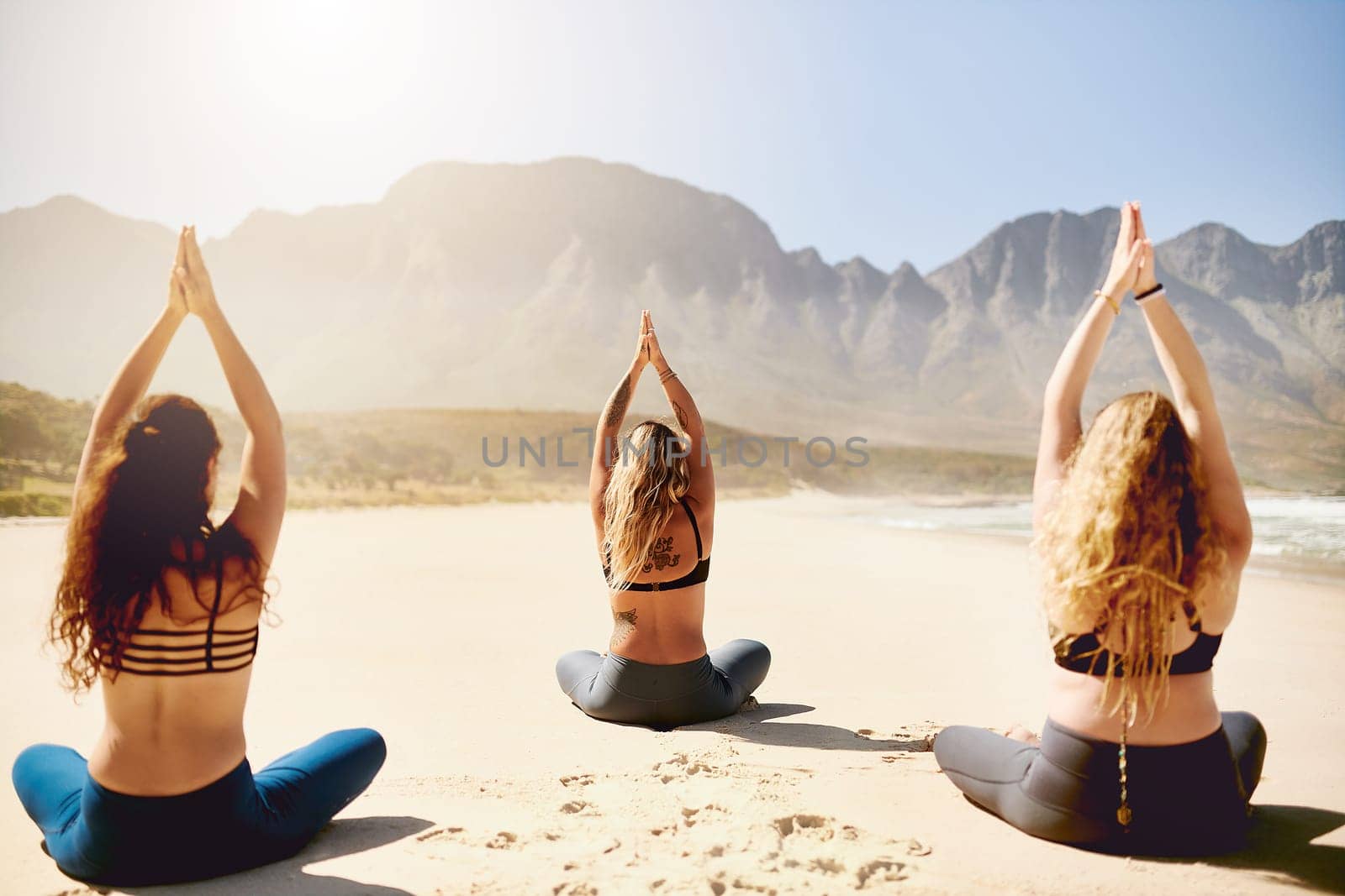 Water your roots so your soul can blossom. Rearview shot of three young women practising yoga on the beach. by YuriArcurs