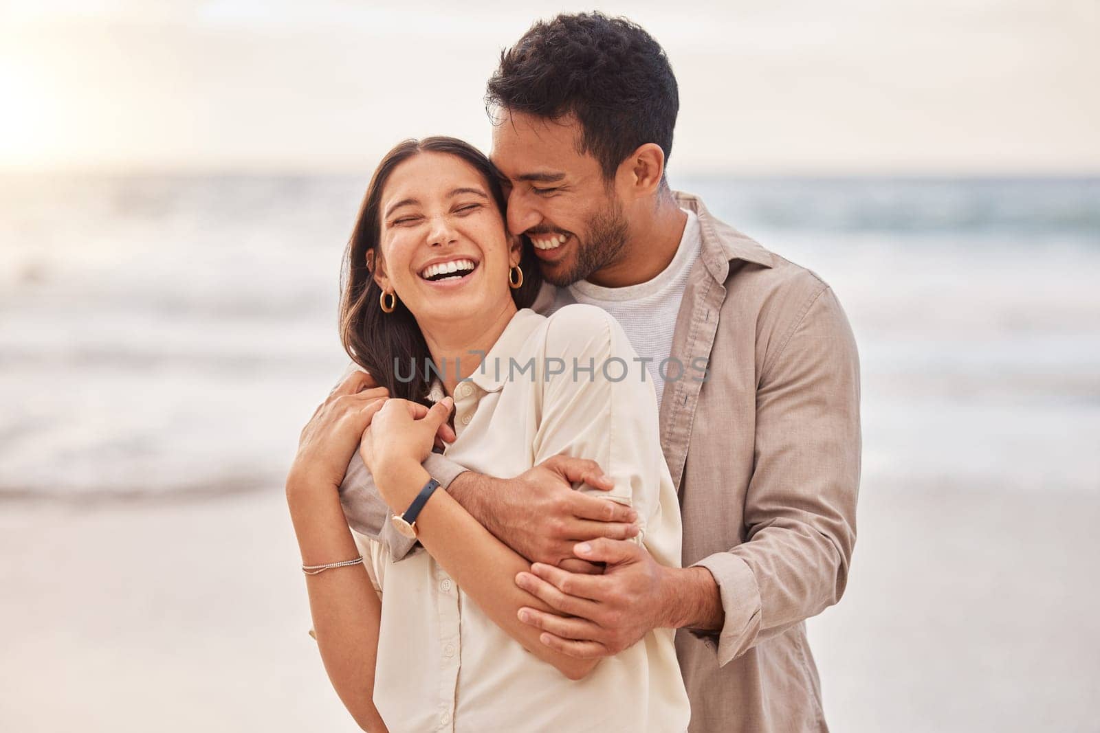 Together, beach and happiness with hug on holiday for having fun with sunset for the weekend. Couple, vacation and laughing with face at the ocean for travel in the summer for a relaxing time