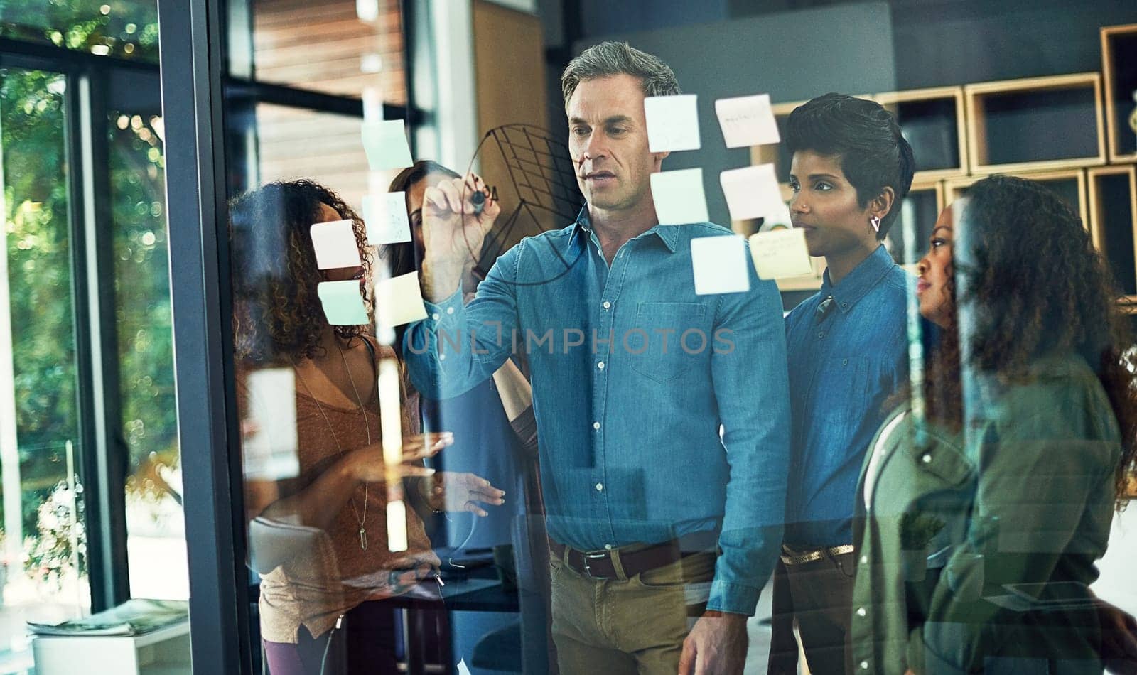 Mapping out an approach to reaching their goals. a group of businesspeople brainstorming with notes on a glass wall in an office